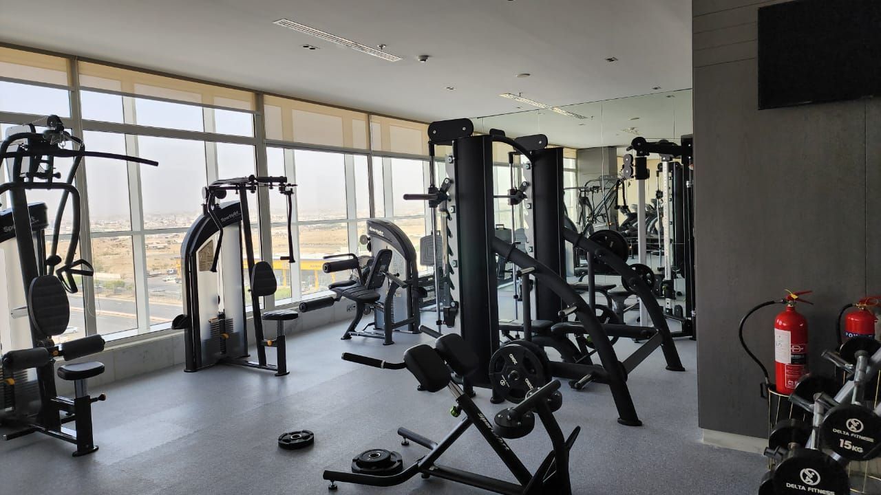 Modern gym with weight machines, benches, and large windows overlooking the city.