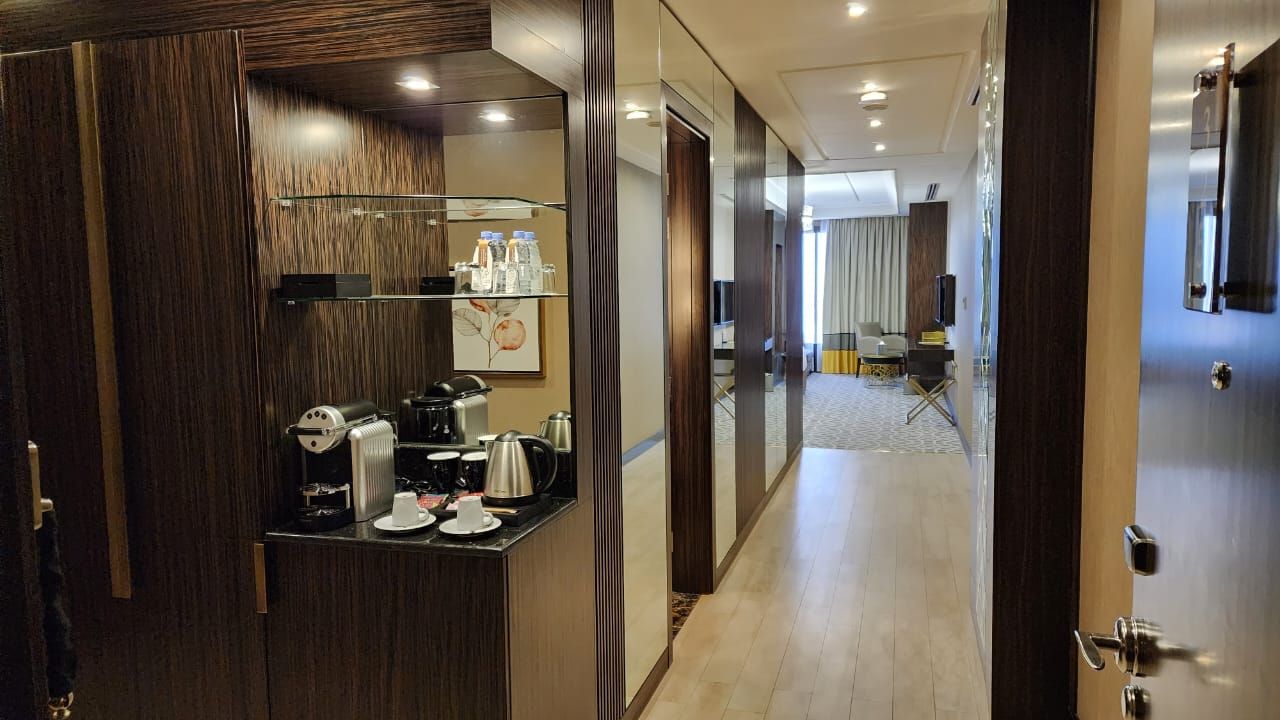 Hotel room hallway with wood paneling, a coffee station, and a bright corridor leading to a window