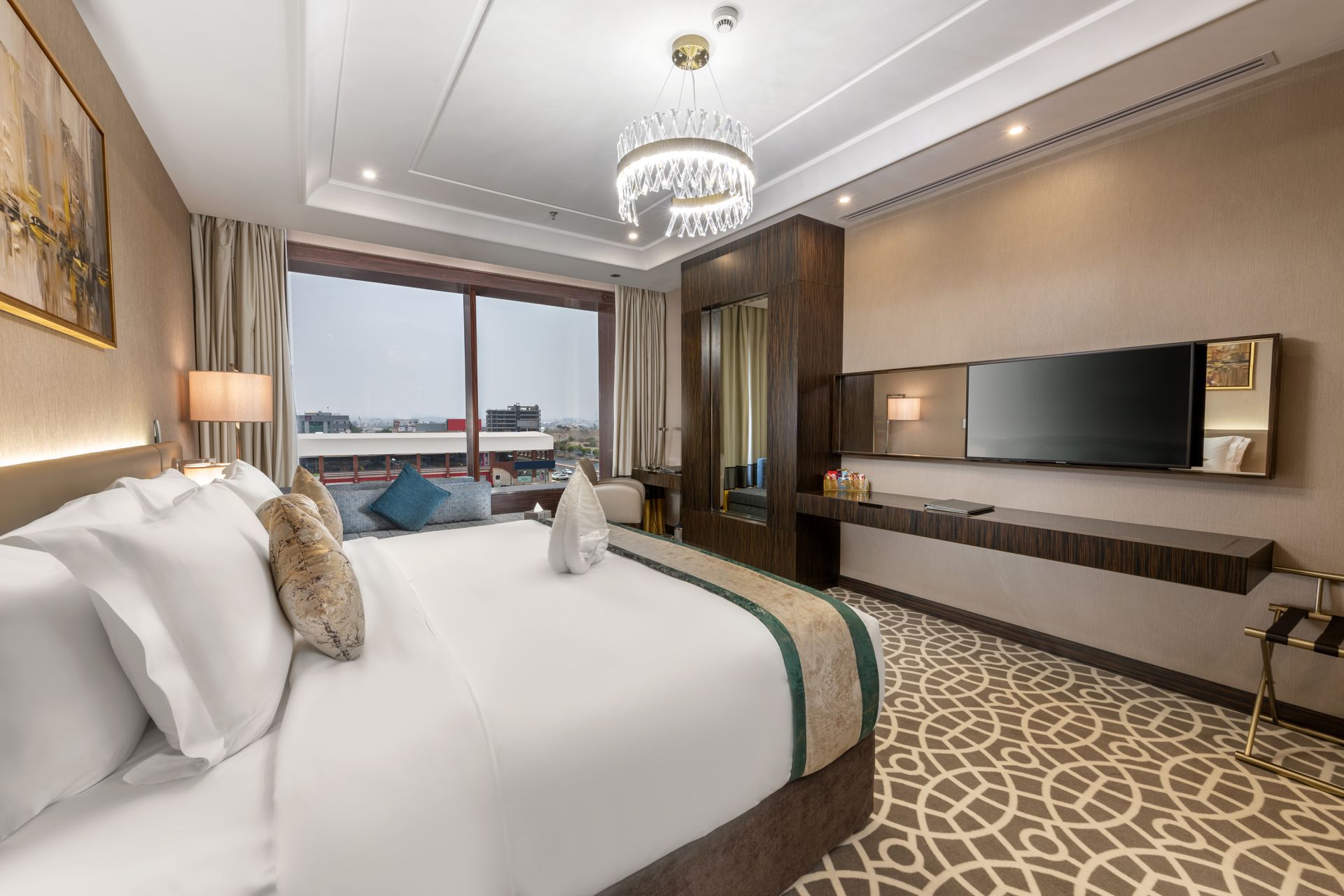Luxurious hotel room with king bed, chandelier, wall TV, and marina view through large windows