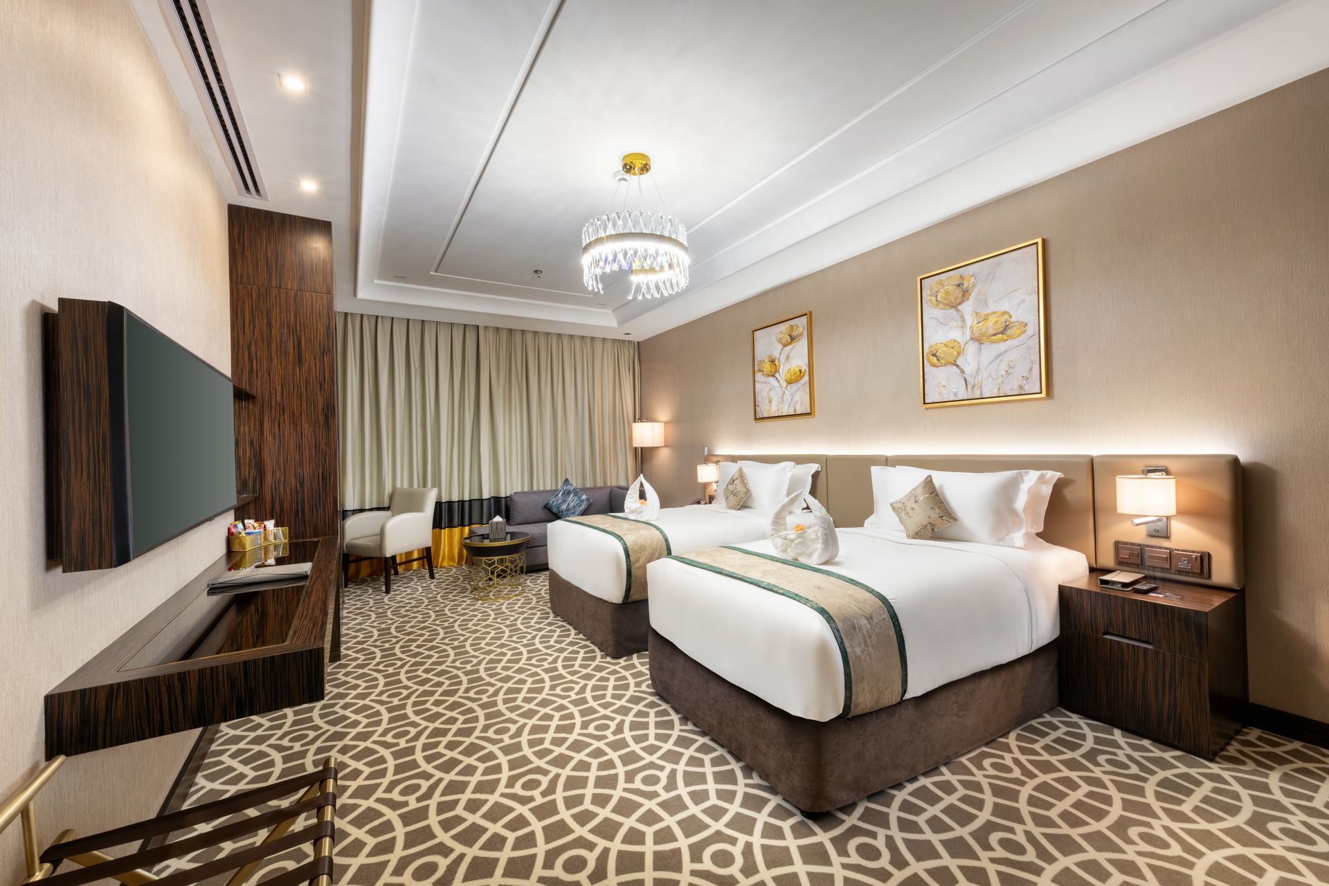 Modern hotel room with two neatly made beds, chandelier, patterned carpet, and curtains by the window