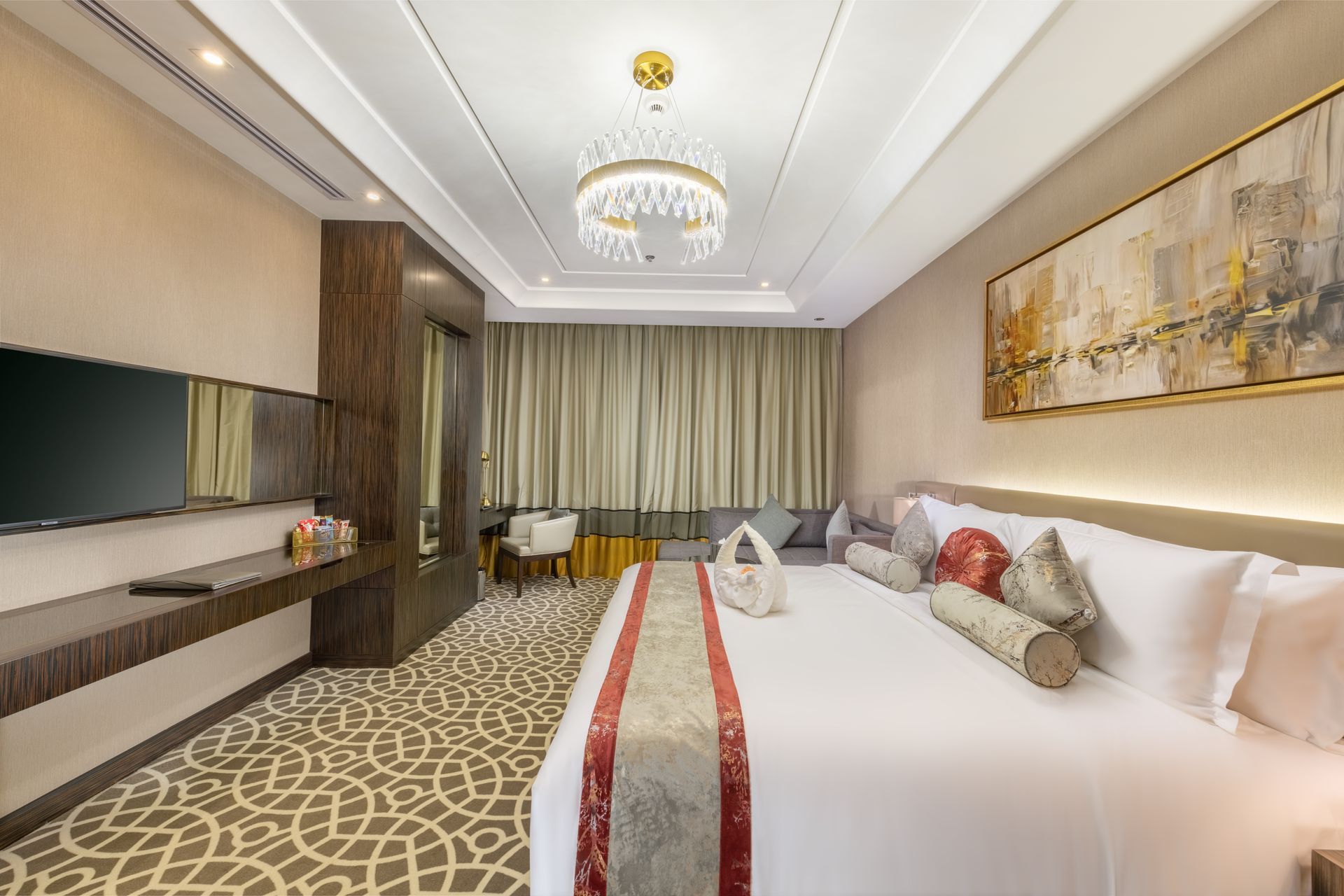 Modern hotel bedroom with a large bed, chandelier, patterned carpet, and wall-mounted TV