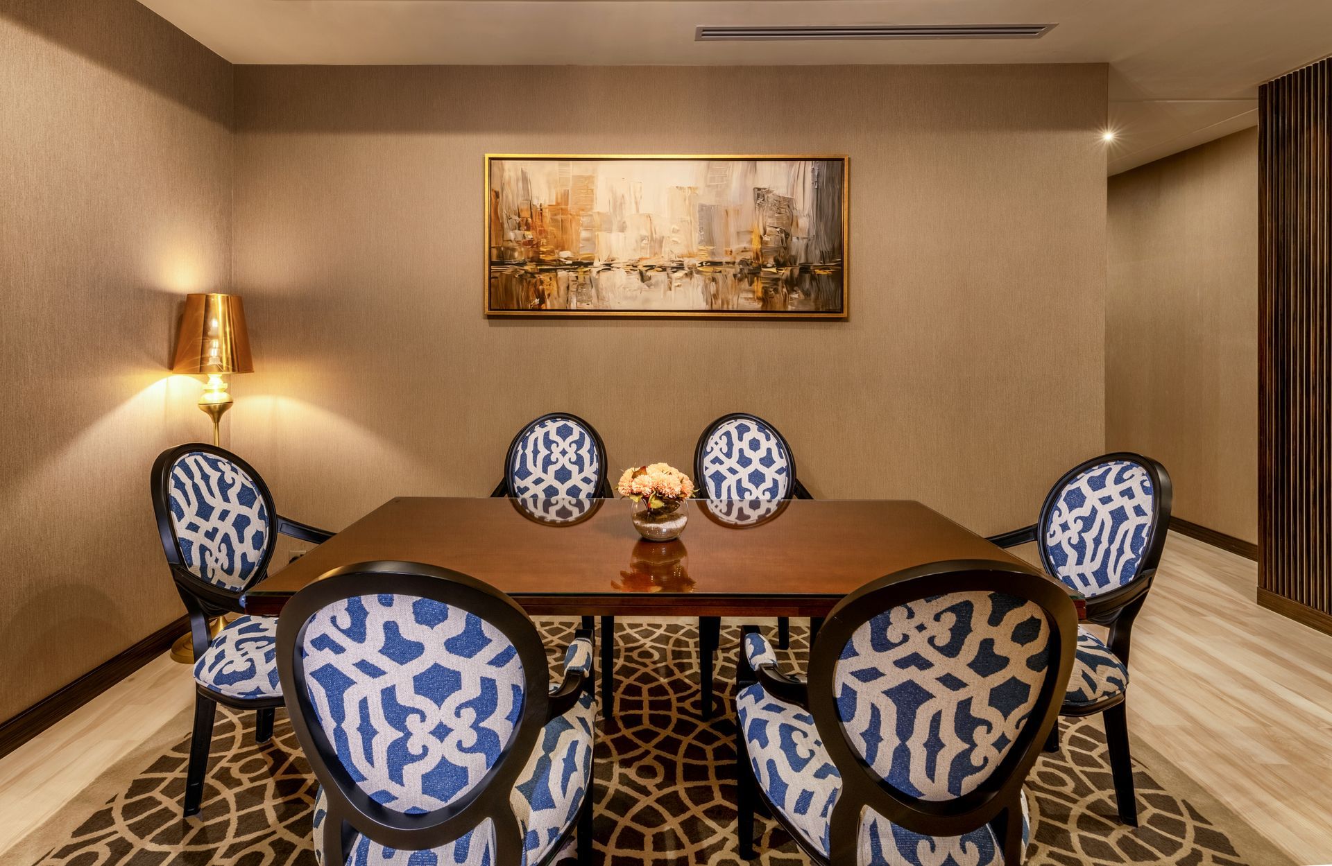 Dining room with a table and six patterned chairs, artwork on the wall, and a lamp.