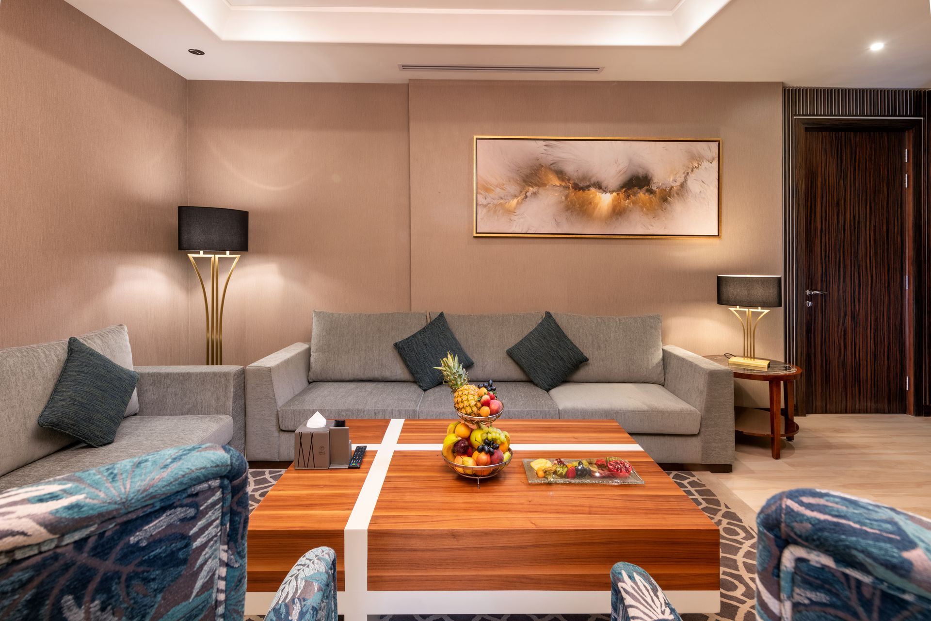 Modern hotel lounge with gray sofas, patterned chairs, wood coffee table, and warm ambient lighting