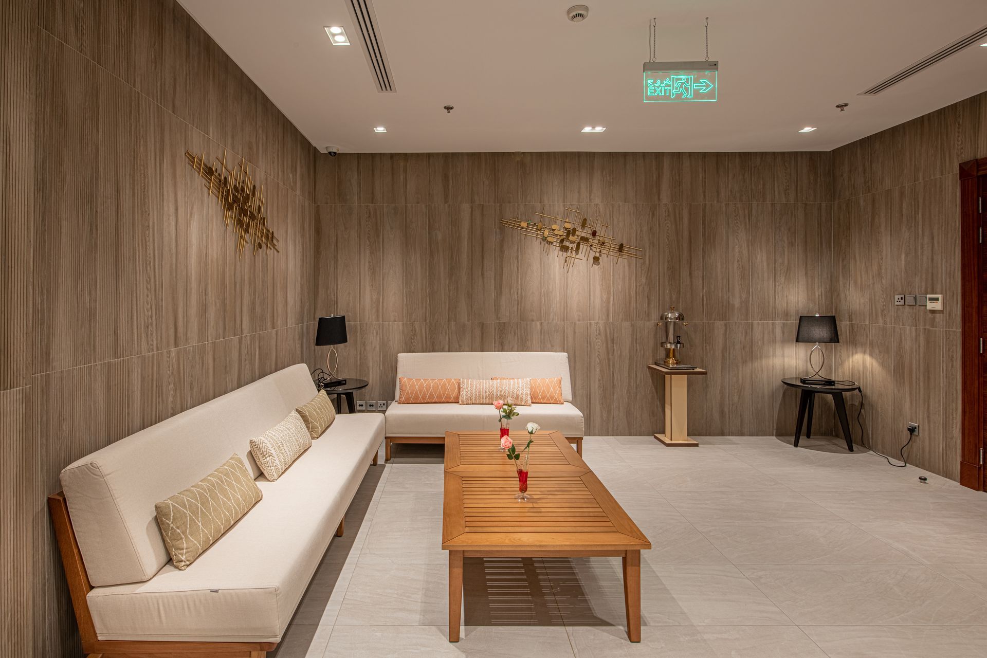 Lounge area with light-colored sofas, wooden coffee table, and decorative wall art. Neutral-toned walls and flooring.