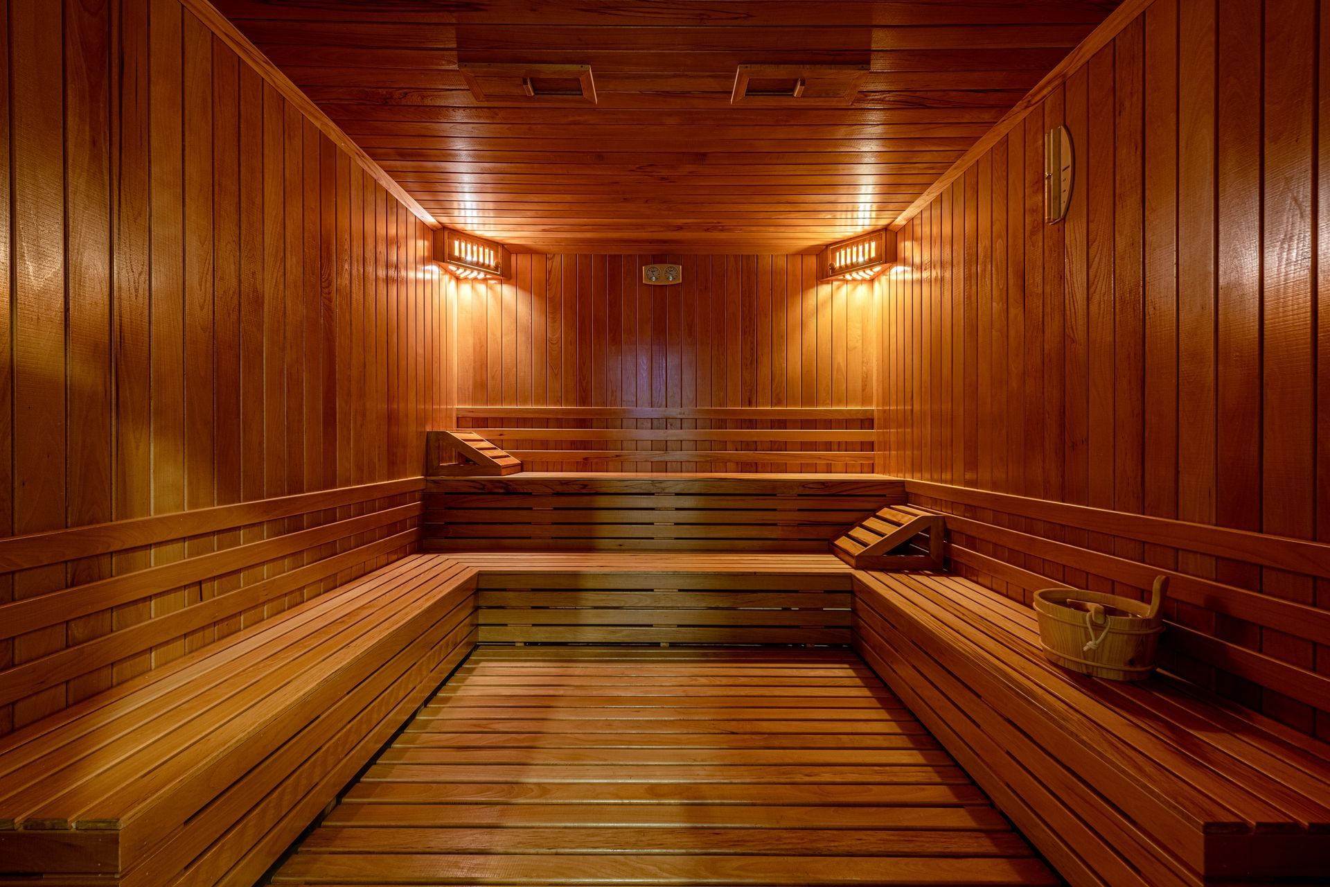 Wooden sauna interior with tiered benches. Warm lighting illuminates the space.