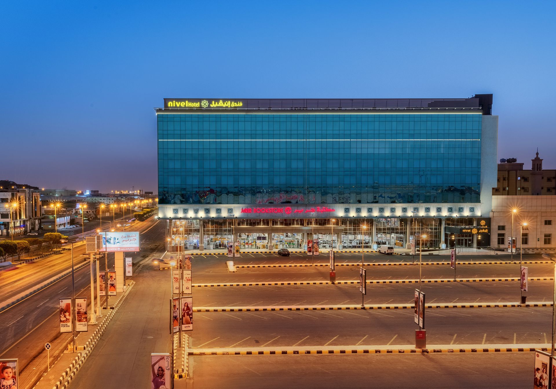 Large glass-fronted building at dusk with lit roads and streetlights in front