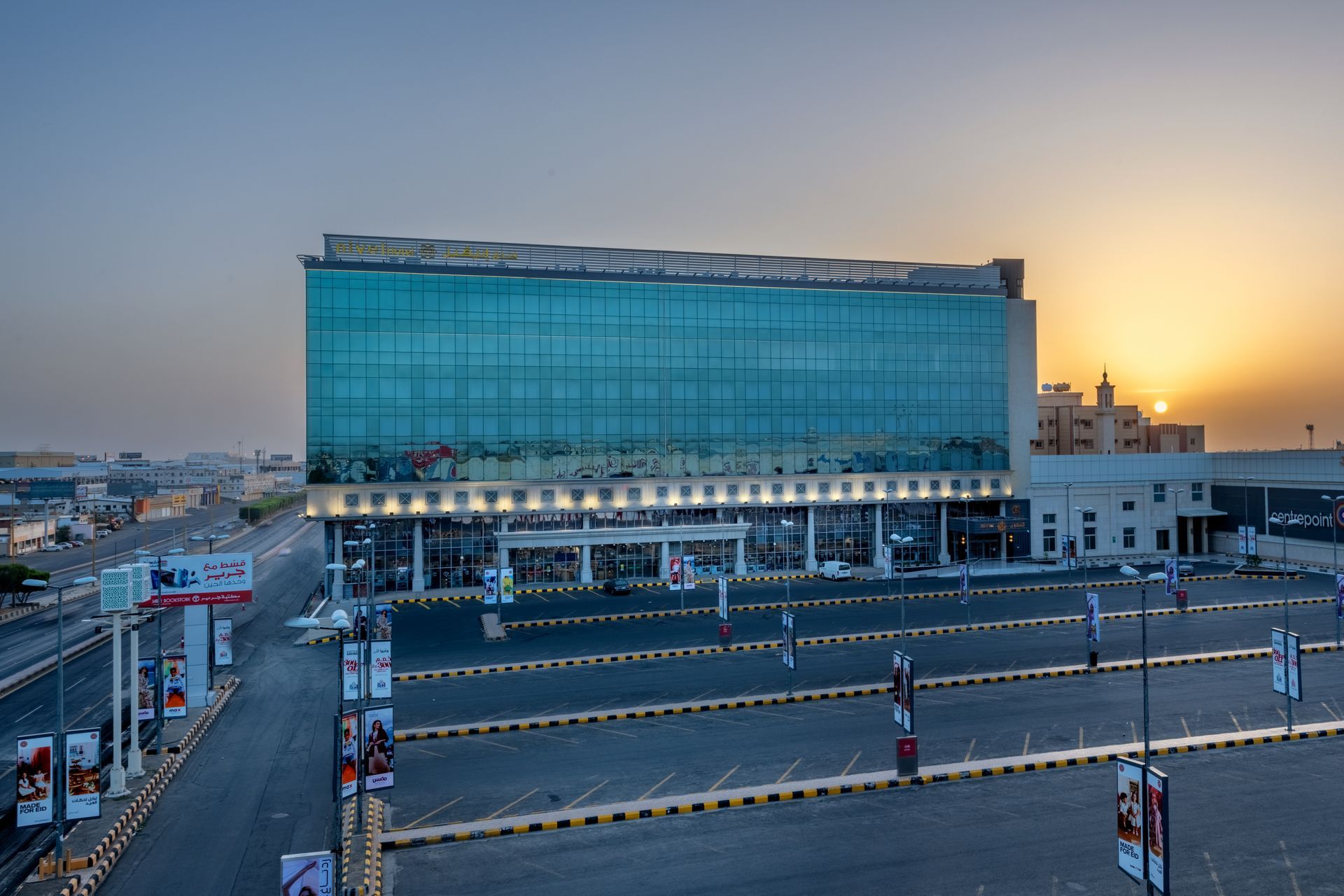 Modern glass-fronted building at sunset beside a mostly empty road with traffic barriers