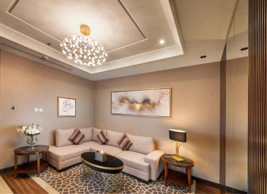 Elegant beige living room with sectional sofa, chandelier, side table, and abstract wall art