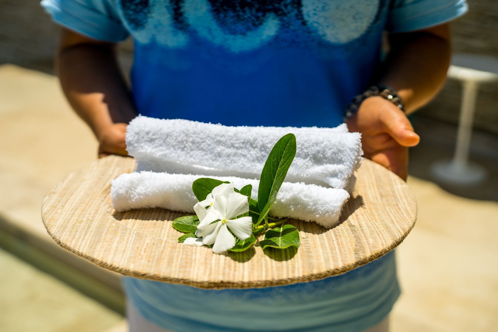 A person is holding a wooden plate with towels and flowers on it.