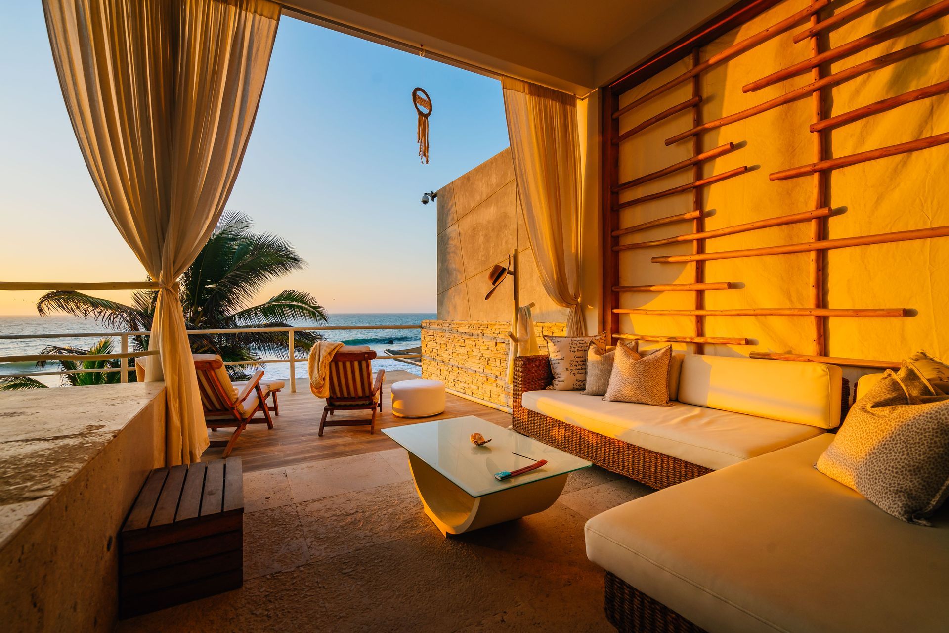 A living room with a couch , table , chairs and curtains overlooking the ocean.