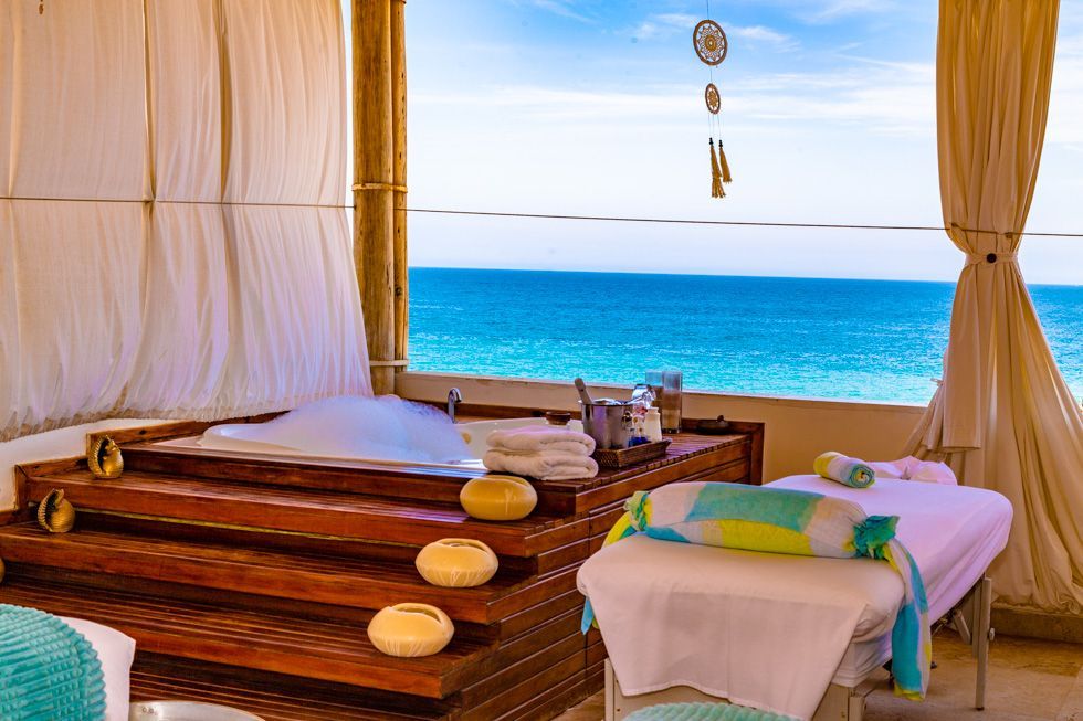 A spa with a jacuzzi and massage tables with a view of the ocean.