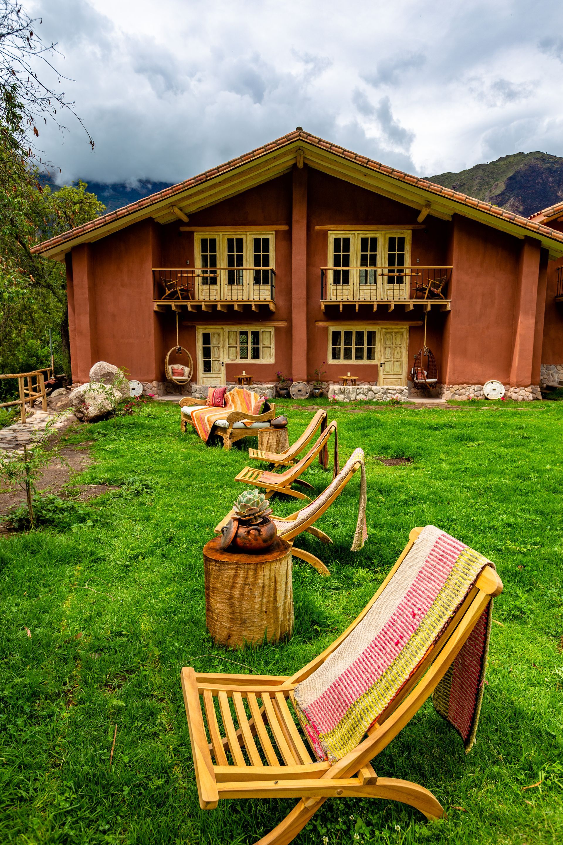 There are many chairs in the grass in front of a house.