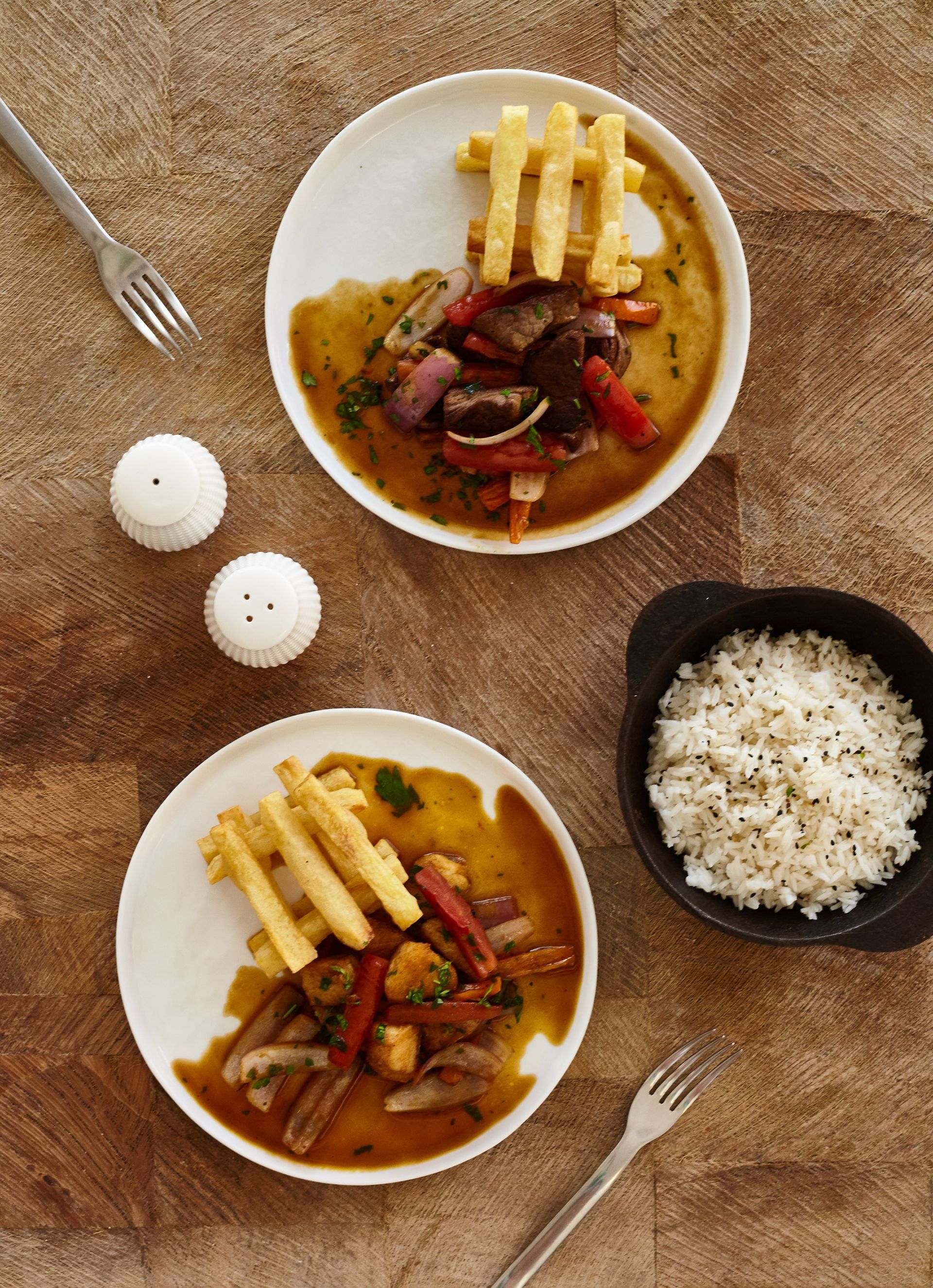 Two plates of food with rice and french fries on a table.