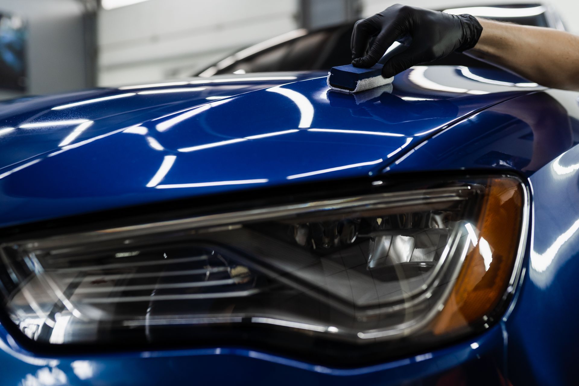 Hand polishing a blue car hood and headlight with a microfiber cloth