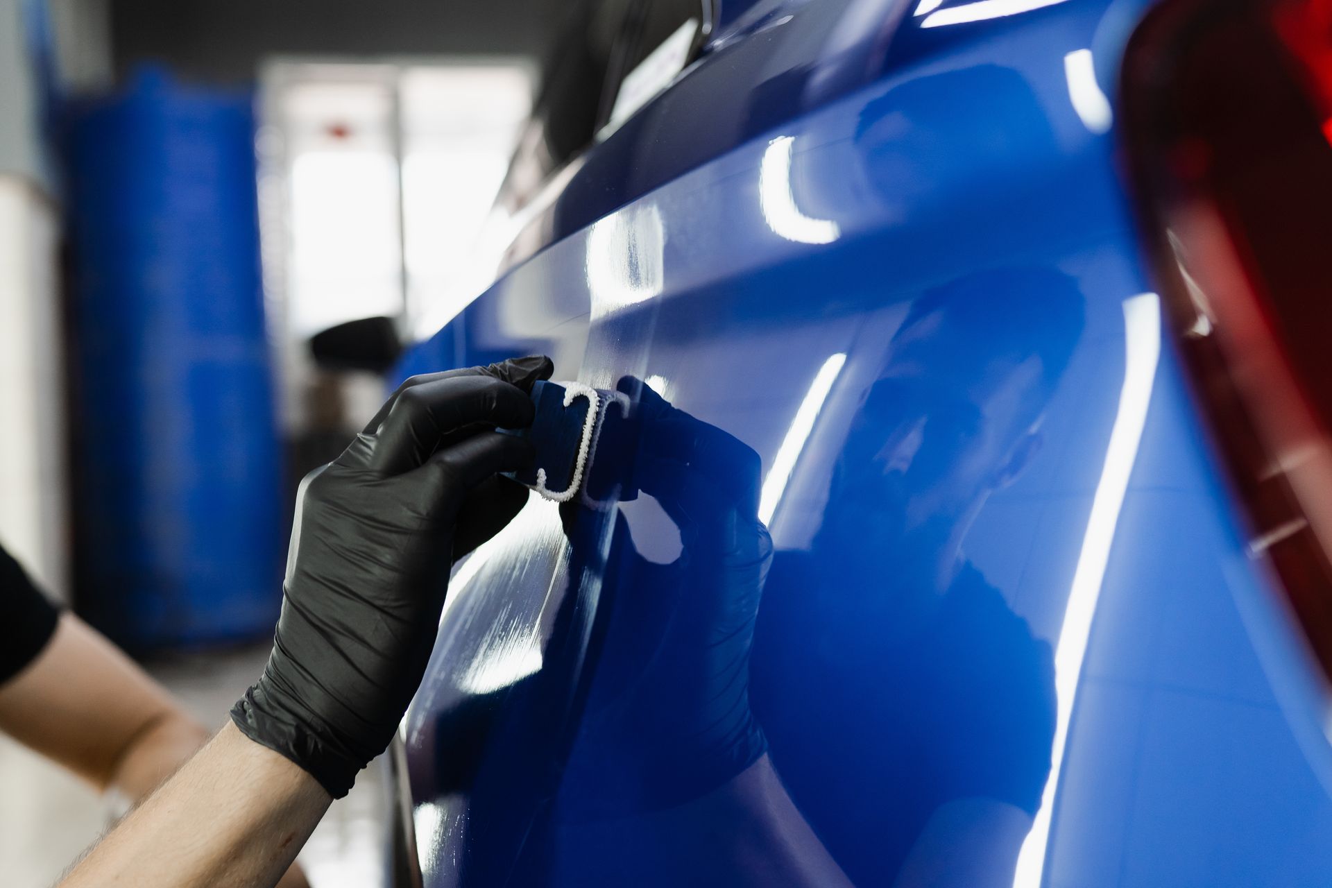Gloved hand polishing a glossy blue car panel in an auto body shop