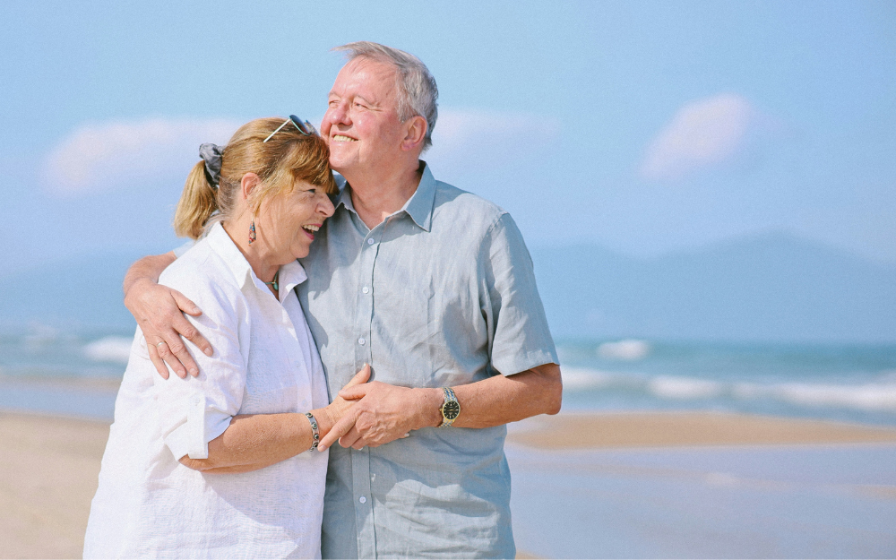 Older Couple Embracing on a Sunny Beach — Midcoast Financial Planning Group in Tuncurry, NSW