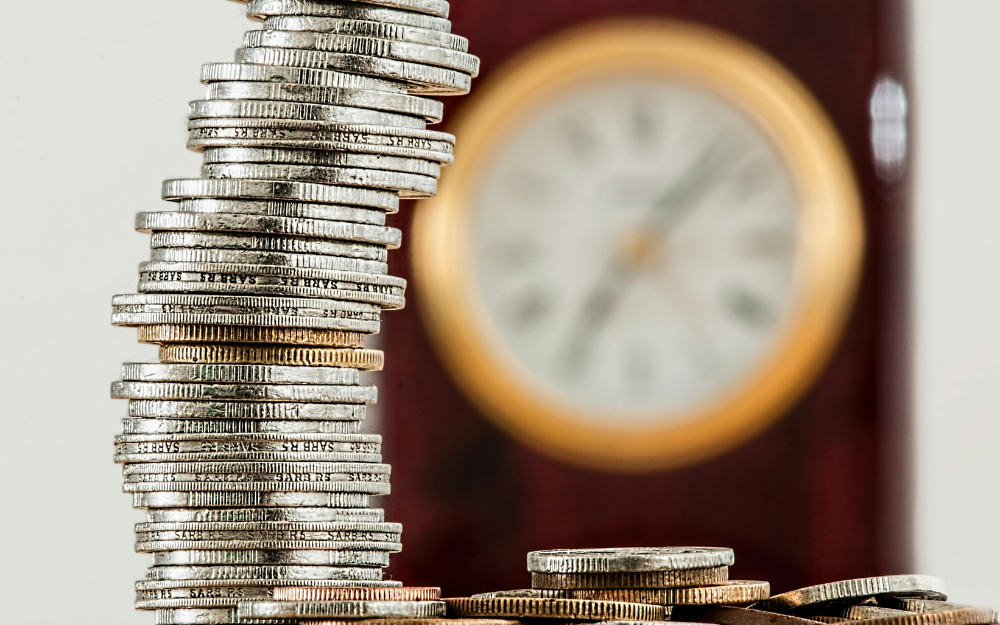 Stack of Coins Beside a Blurred Clock — Midcoast Financial Planning Group in Tuncurry, NSW