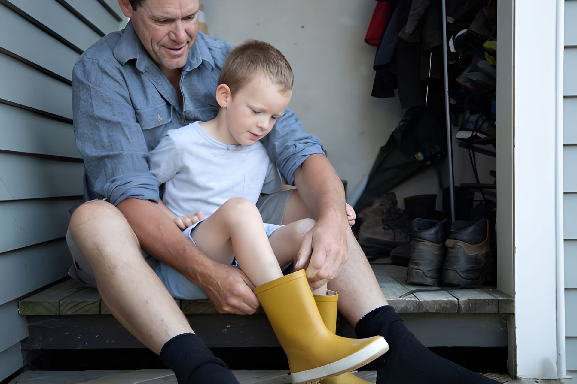 Man helping child put on yellow rain boots — Midcoast Financial Planning Group in Tuncurry, NSW