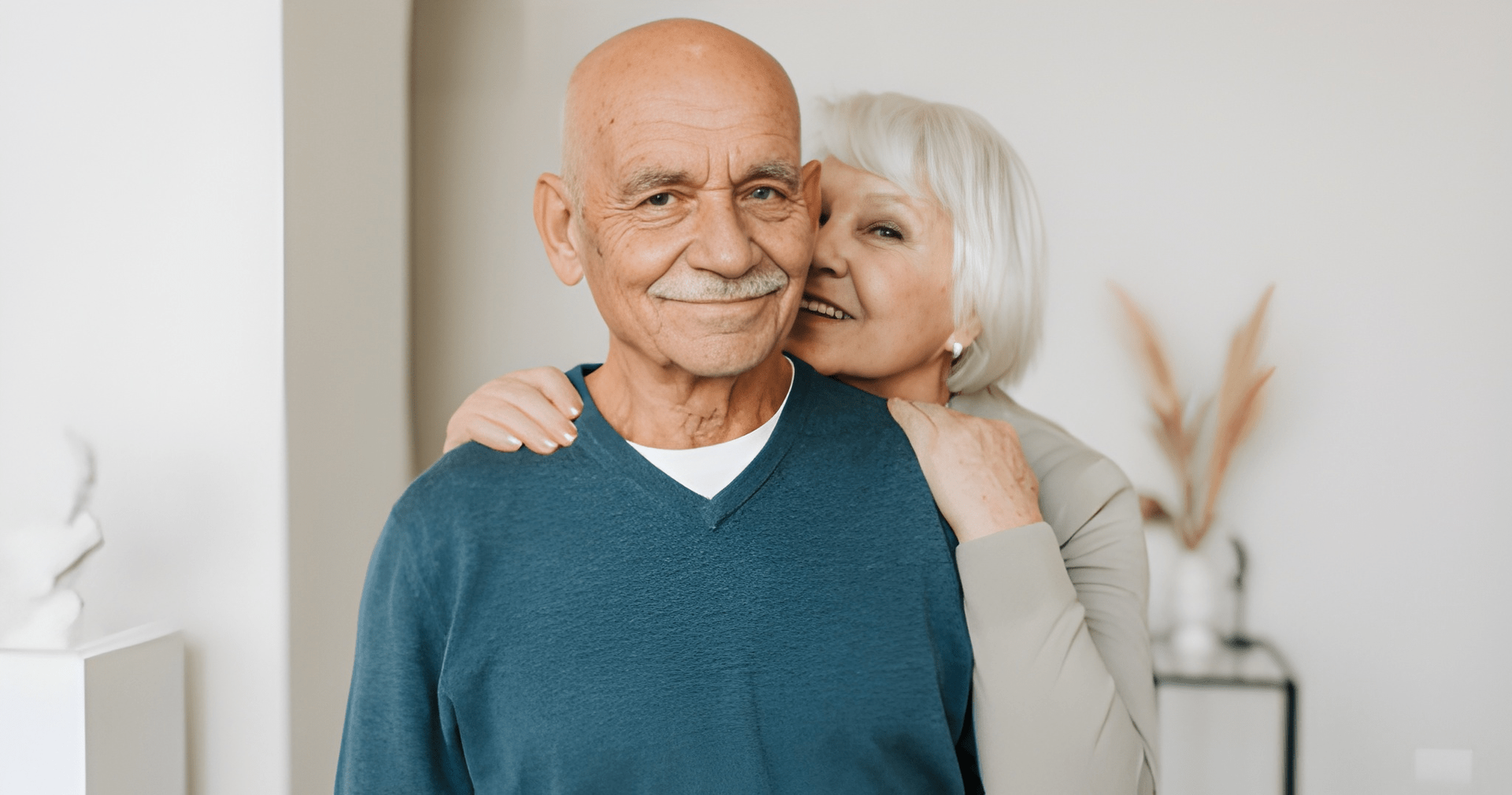 Elderly Couple Smiling, Woman With Her Arms Around Man, Inside, Near a Wall — Midcoast Financial Planning Group in Tuncurry, NSW
