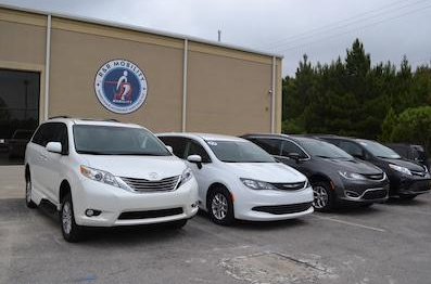 Four parked minivans outside a dealership building on a cloudy day