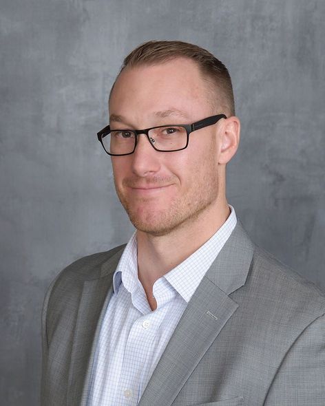 Portrait of a man in a light gray suit and glasses against a gray studio backdrop
