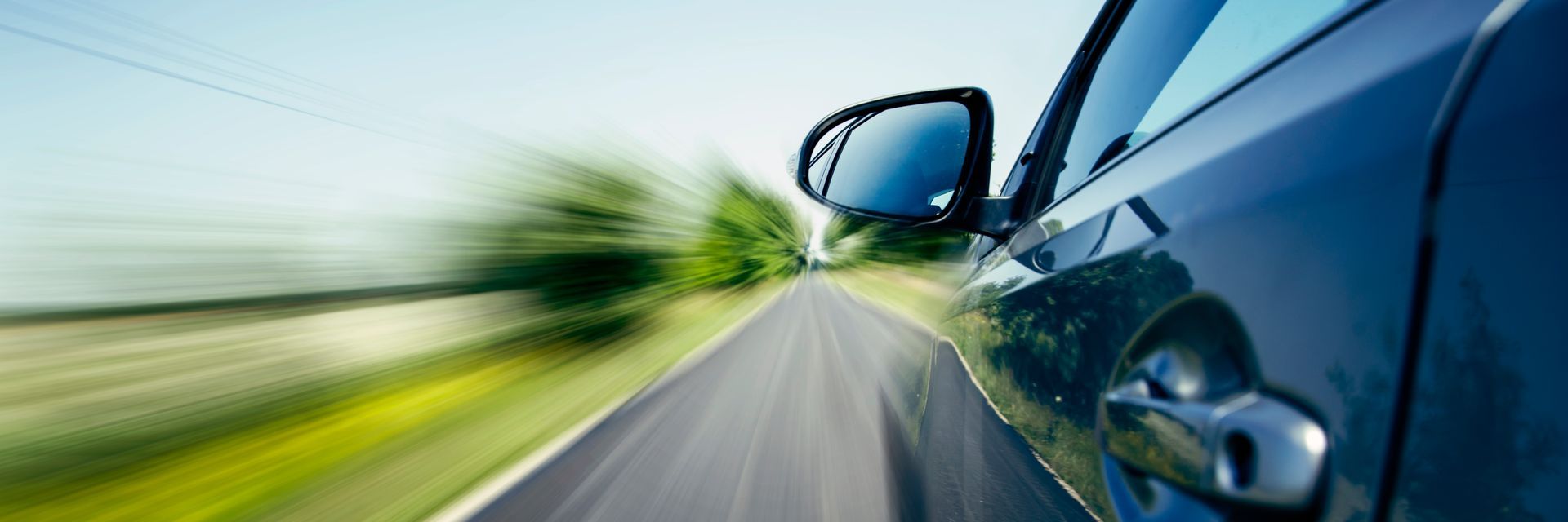 A blue car driving down a country road at high speed, blurred motion effect showing the landscape passing by.