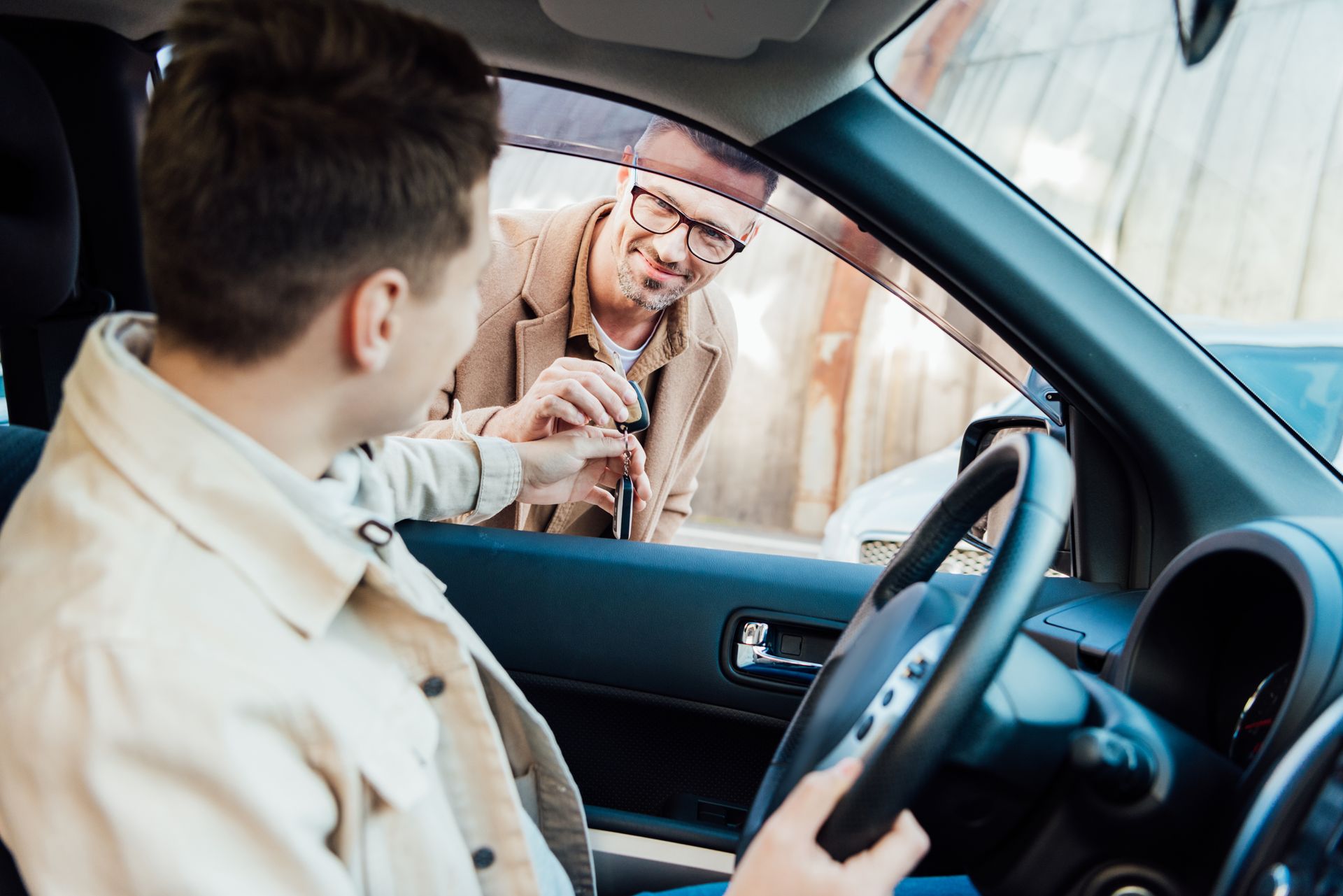 A person in the driver's seat of a car hands a key to another person standing outside the open window.