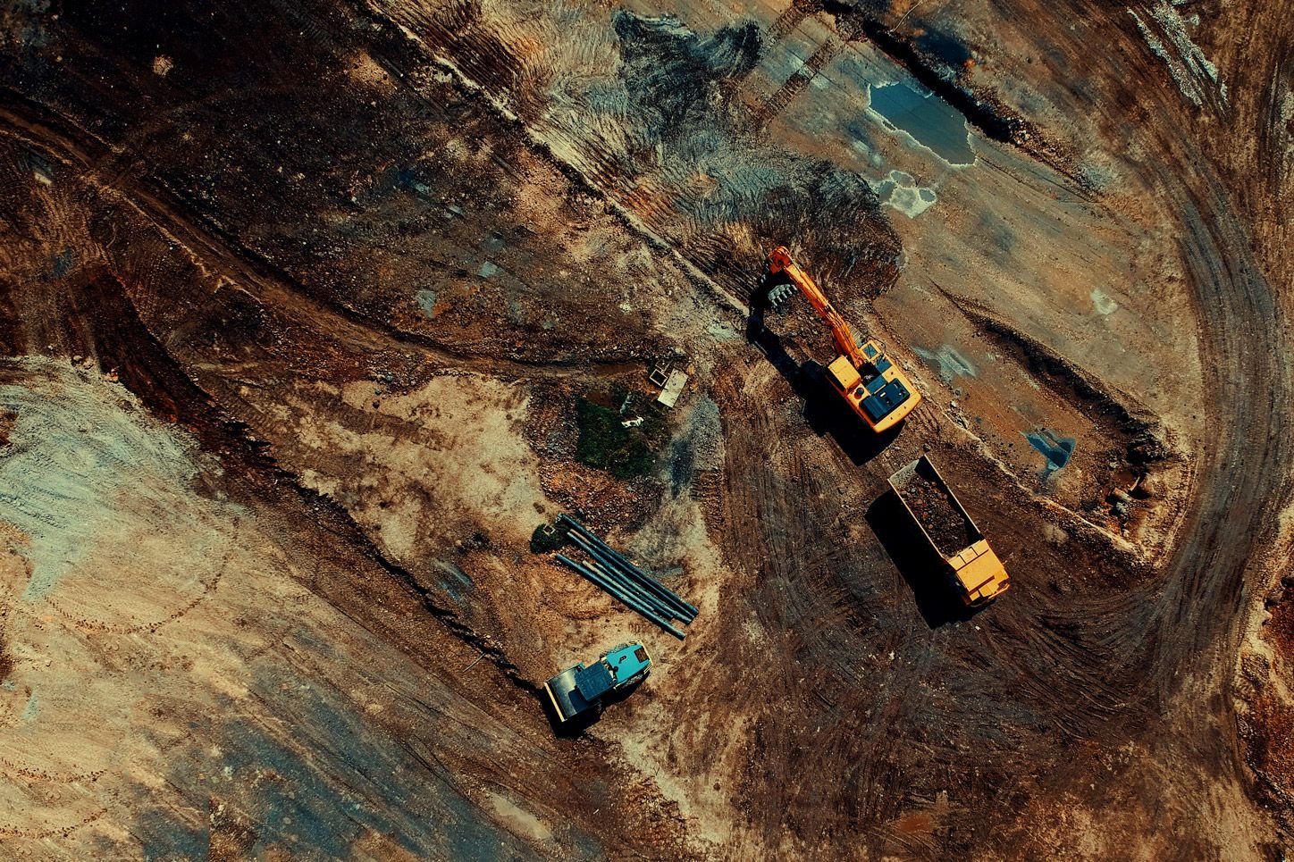 Aerial view of two yellow excavators and a blue dump truck on a dirt construction site