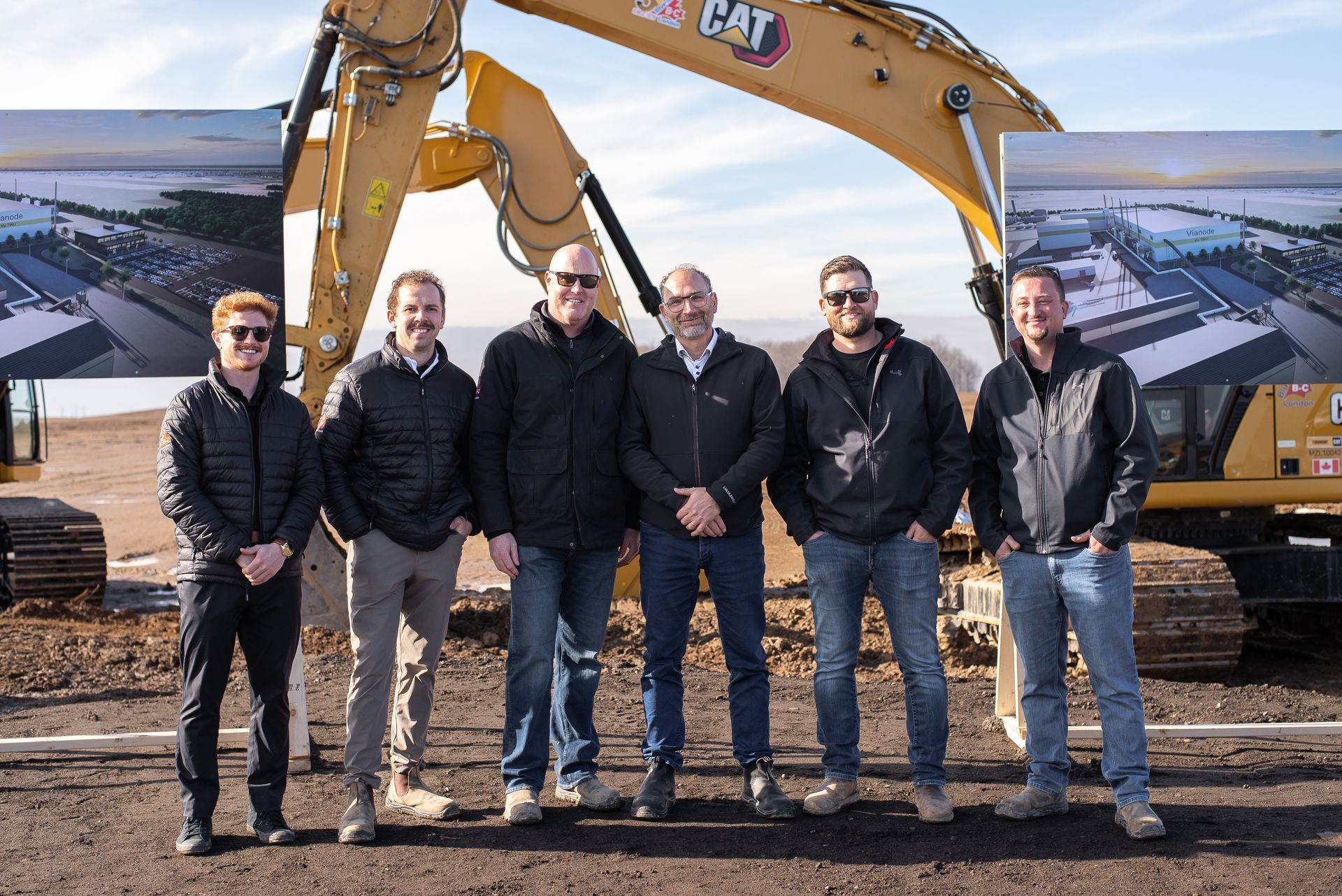 Six people posing in front of a yellow CAT excavator at a construction site