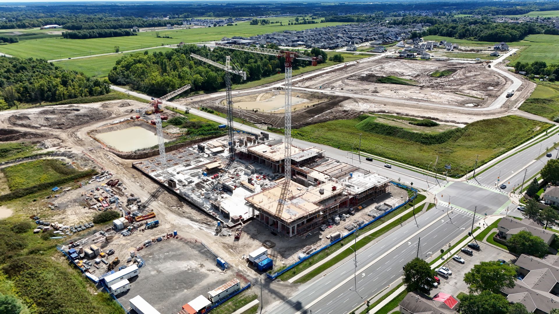 Aerial view of a large construction site with concrete foundation, cranes, and roads beside open fields