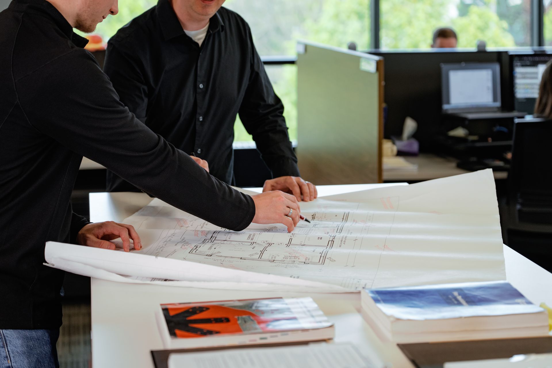 Two people reviewing large blueprint plans on a table in an office workspace