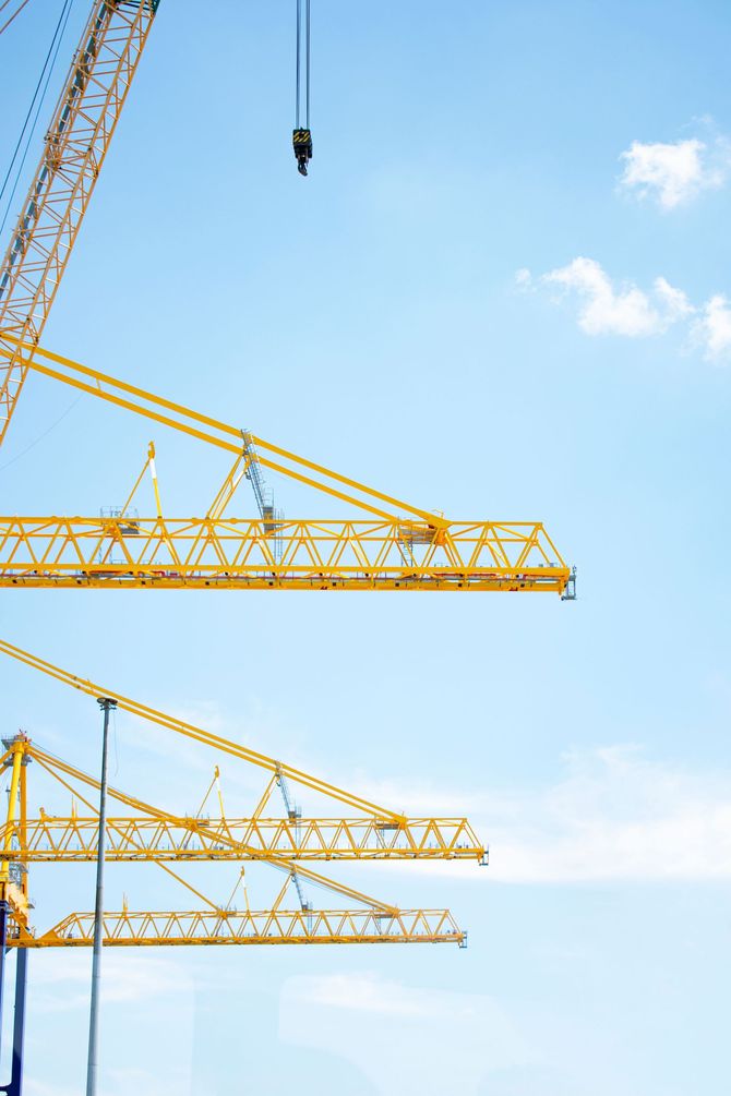 Yellow construction cranes against a blue sky with a hanging hook