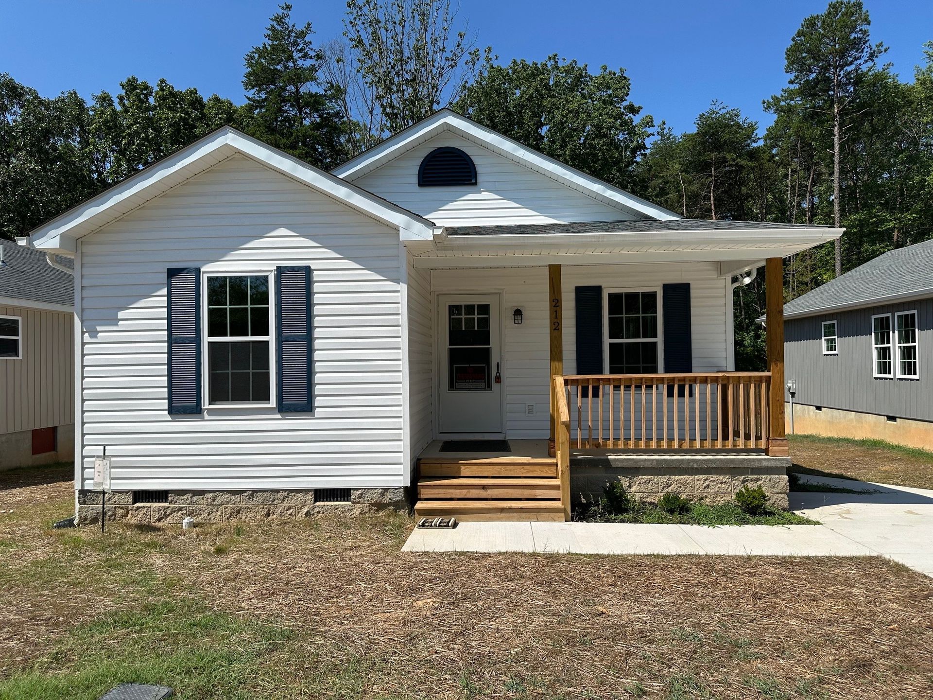 Small white house with black shutters, a front porch, and a concrete walkway under a clear blue sky
