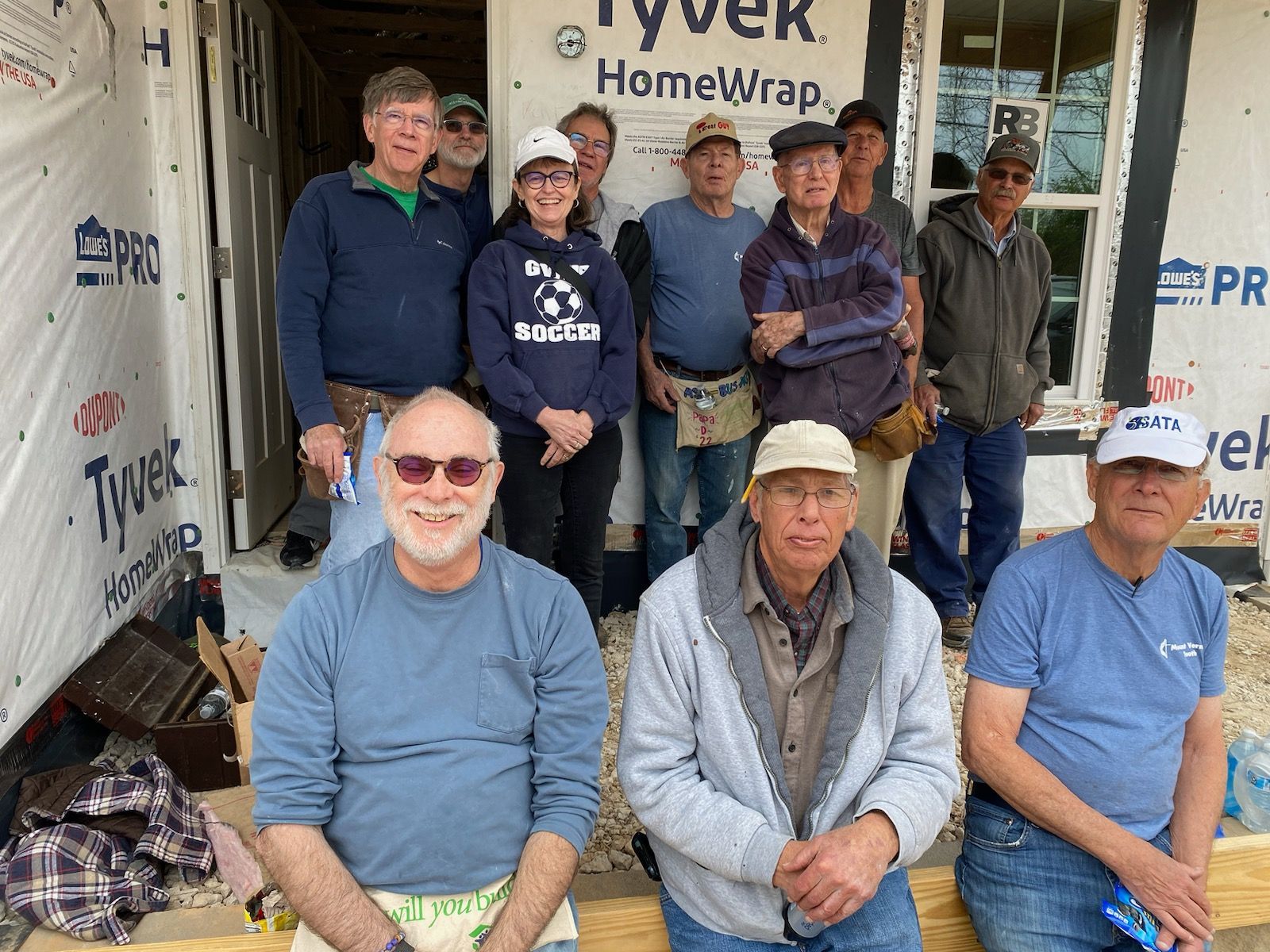 Seven people posing in front of a house under construction with Tyvek HomeWrap visible.