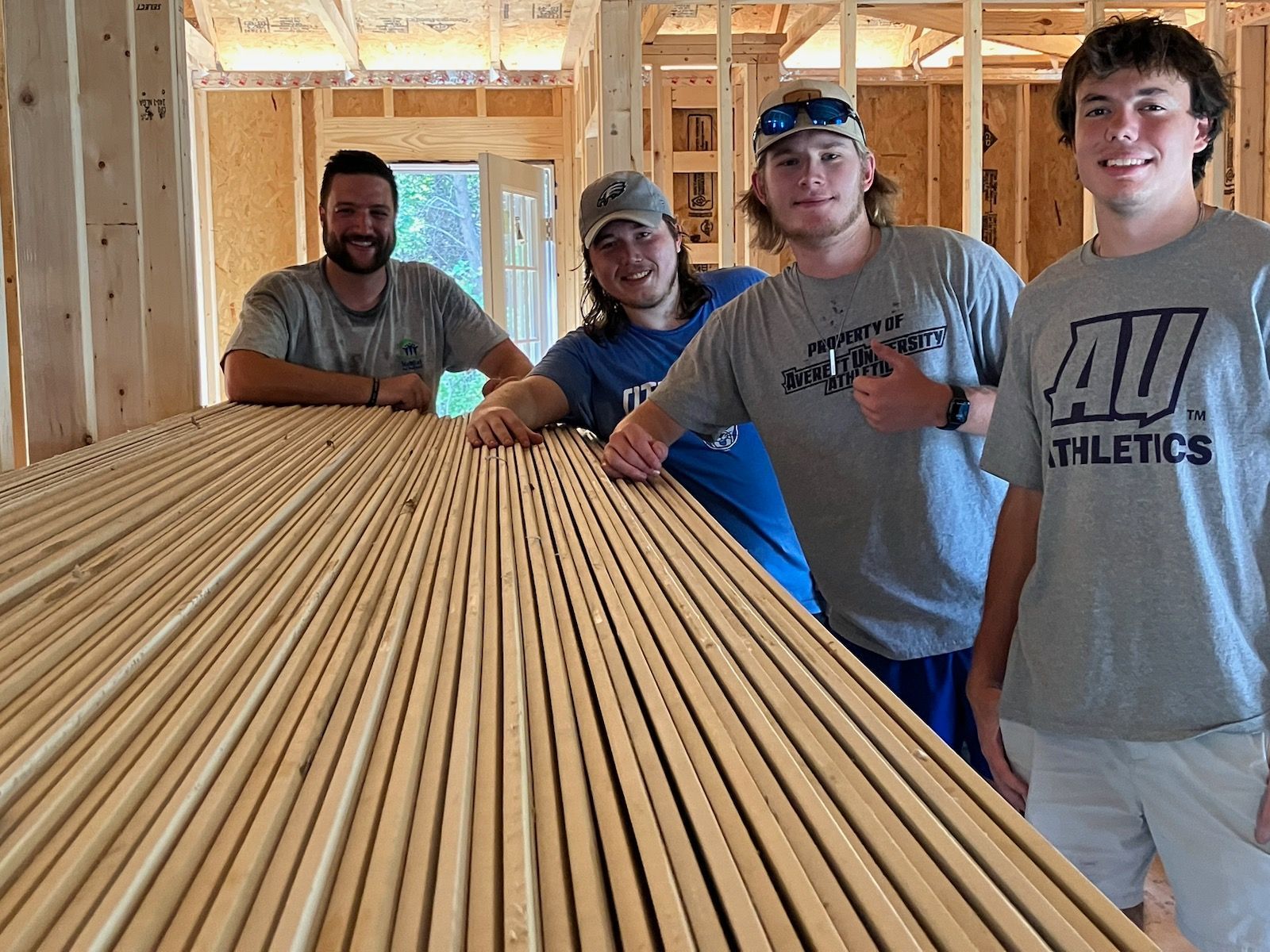 Four men posing inside a framed house under construction, leaning over stacks of lumber.