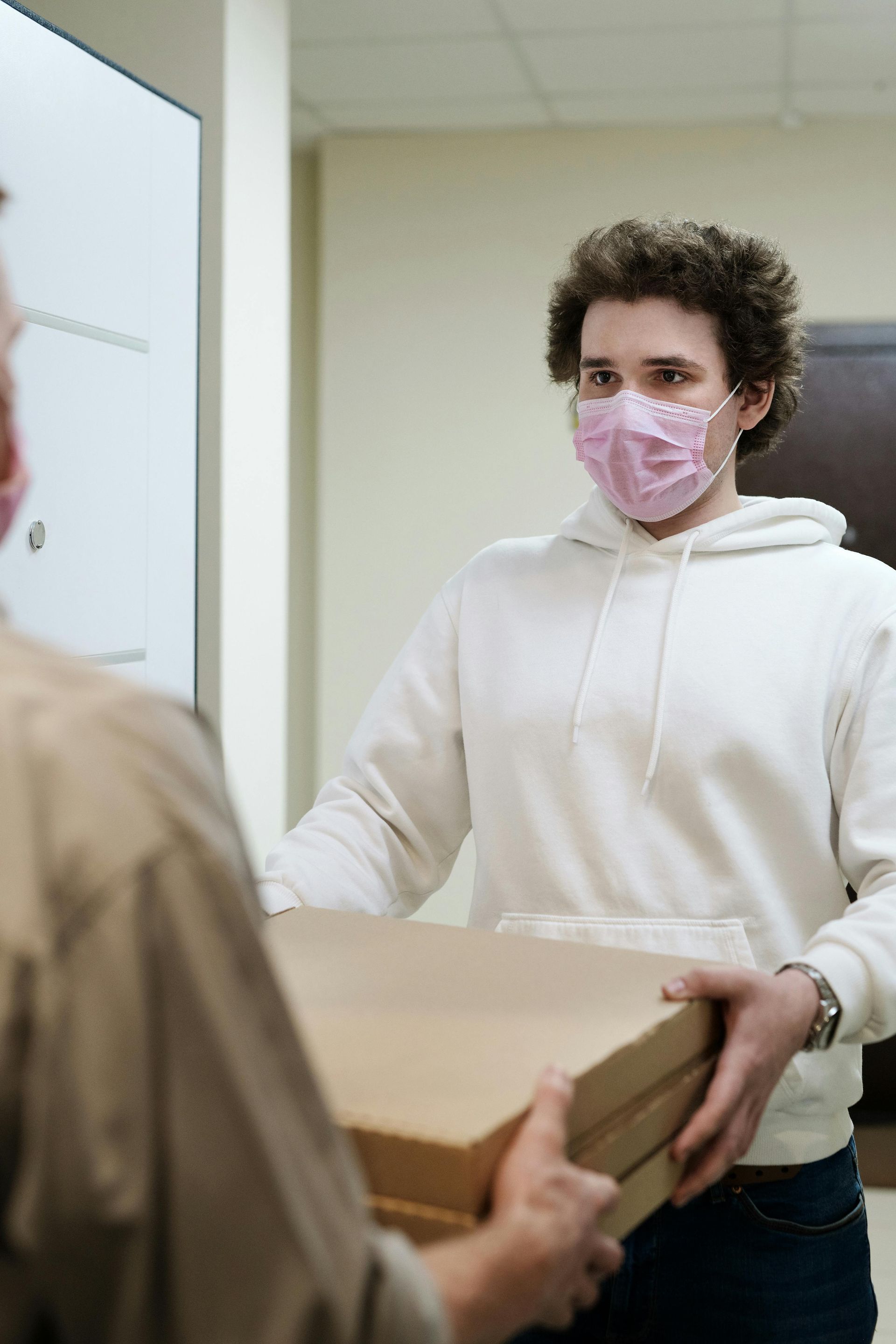 A man wearing a mask is holding a box of pizza.