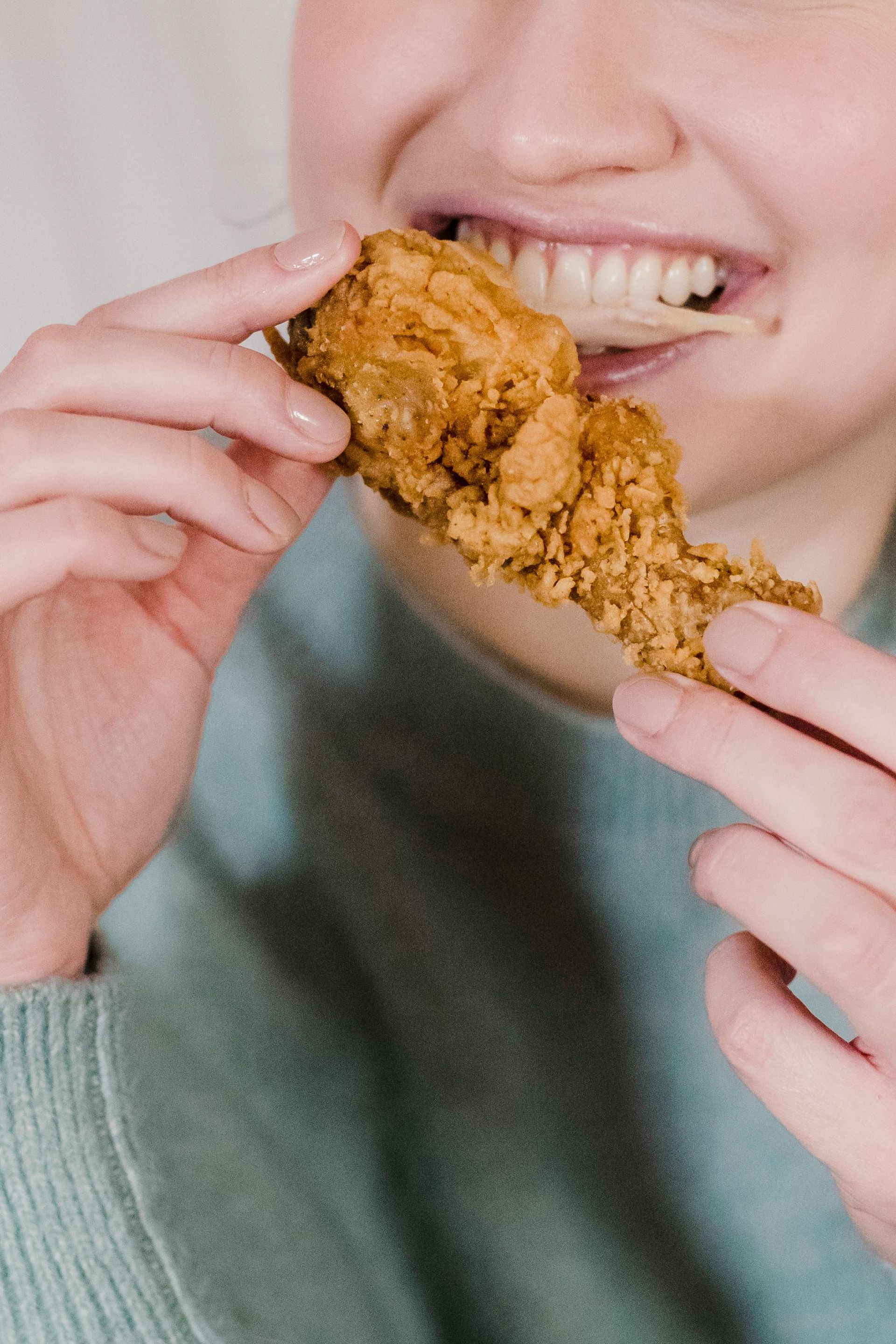 A woman is eating a piece of fried chicken.