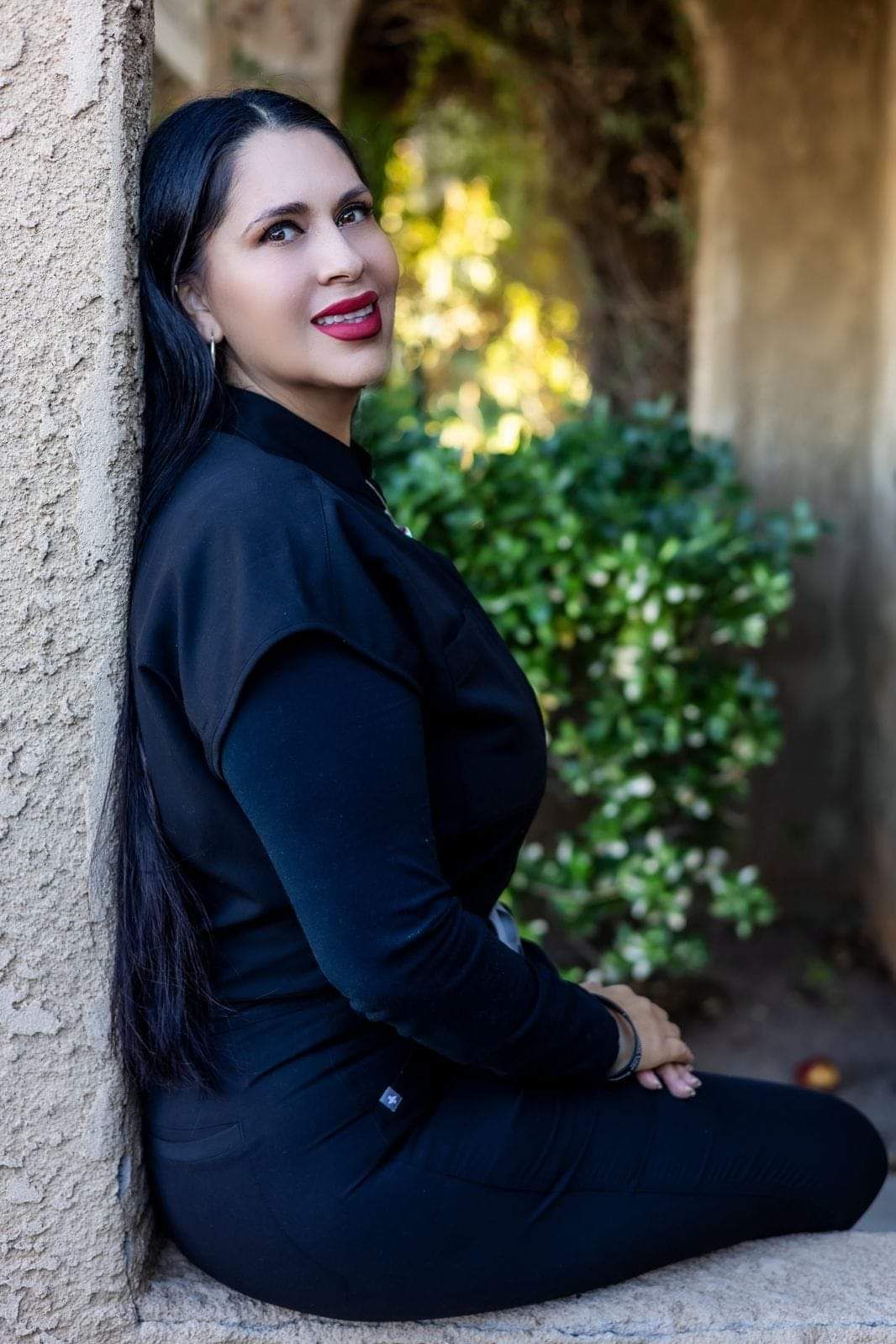 A woman in a black dress is leaning against a wall.