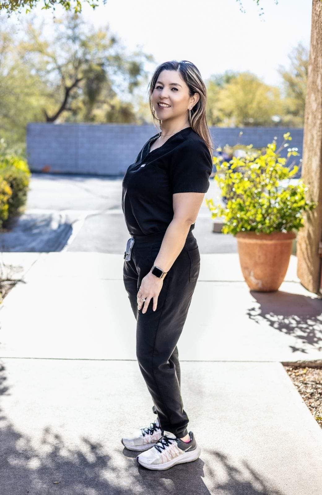 A woman in a black shirt and black pants is standing on a sidewalk.