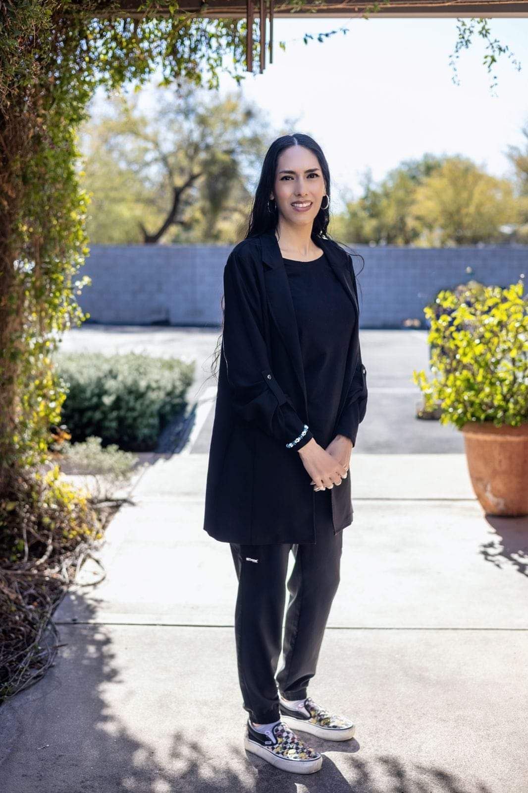 A woman in a black coat and black pants is standing on a sidewalk.