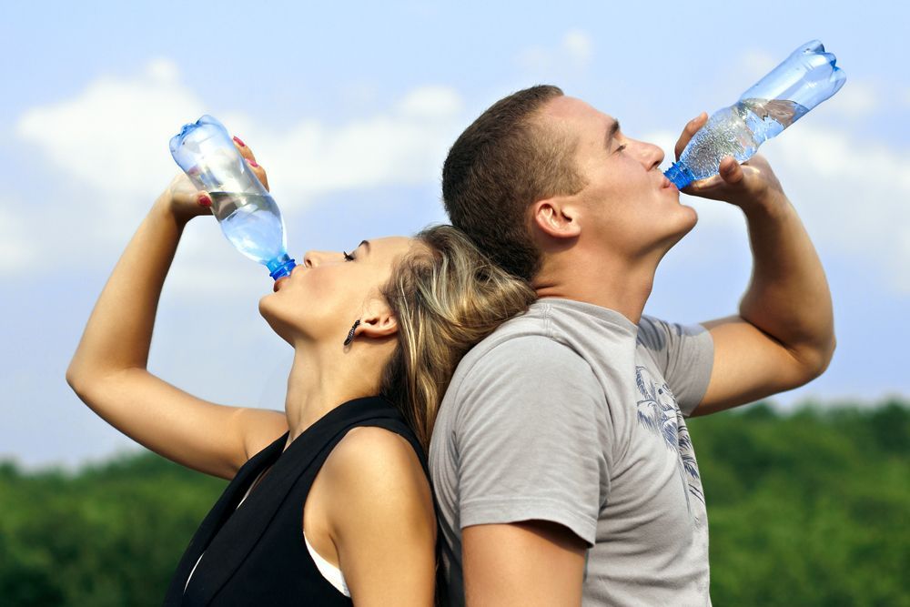A man and a woman drinking water from plastic bottles