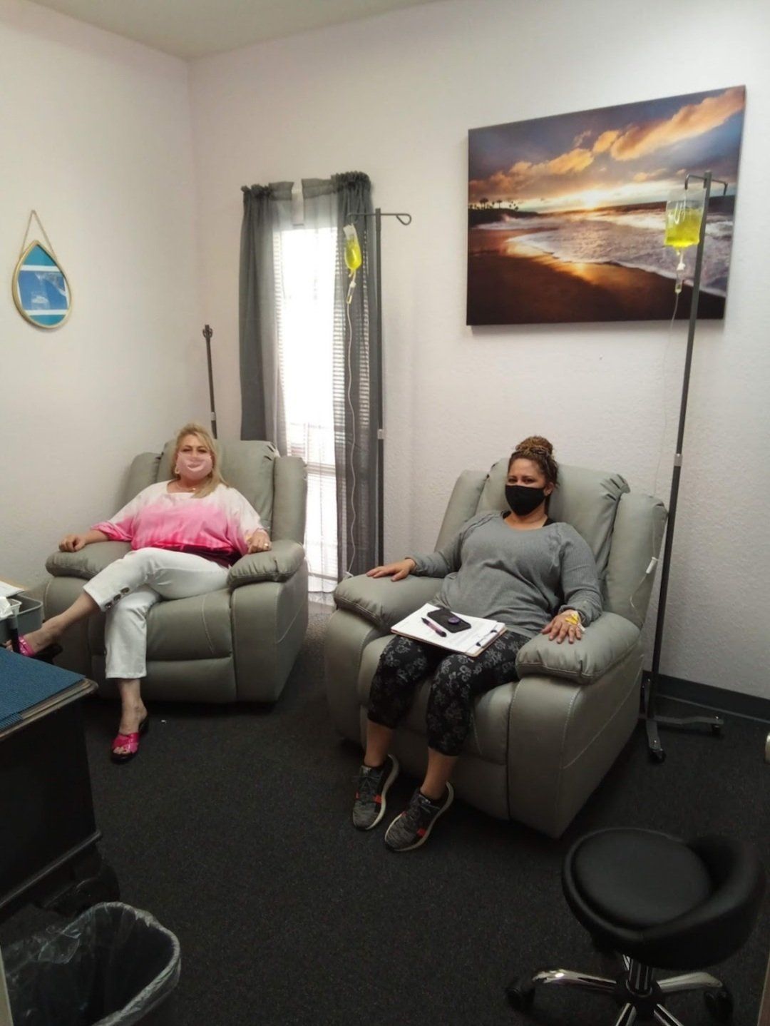 Two women are sitting in chairs in a room with a painting on the wall.