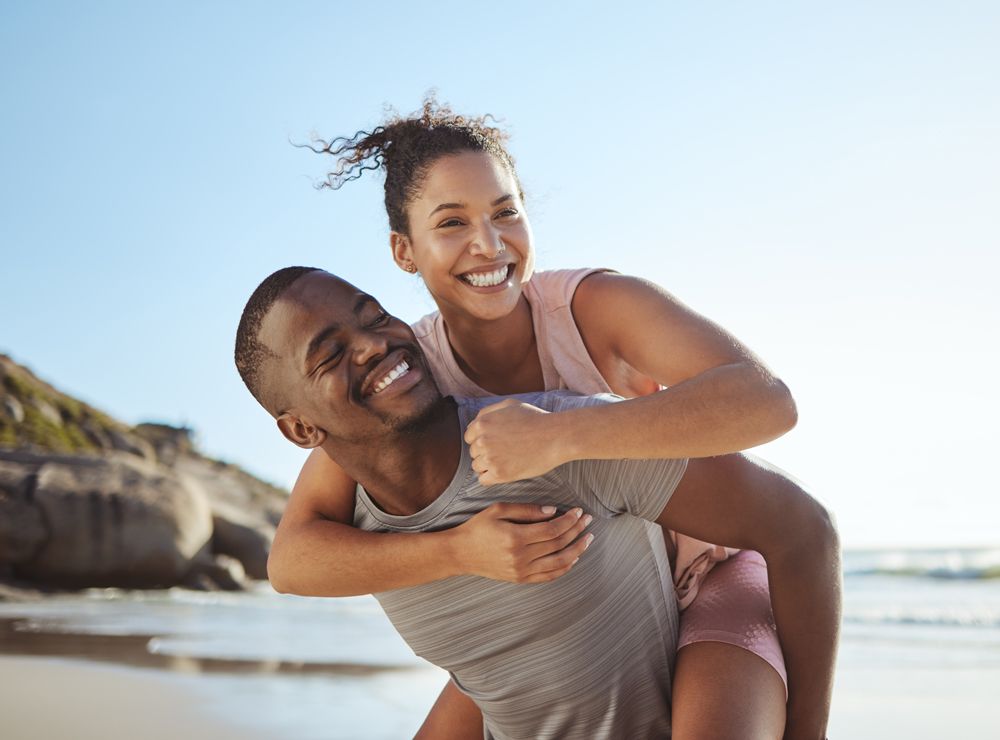 A man is carrying a woman on his back on the beach.