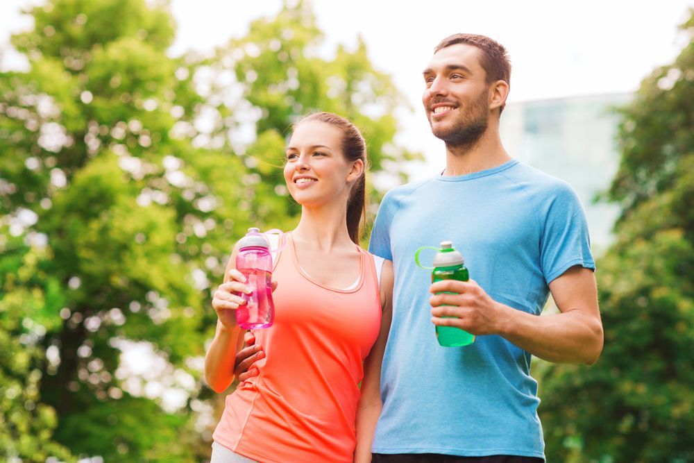 A man and a woman are holding water bottles in a park.