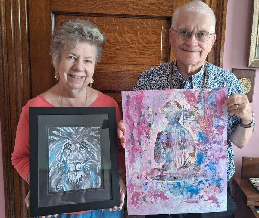 A man and a woman are holding paintings in front of a door.