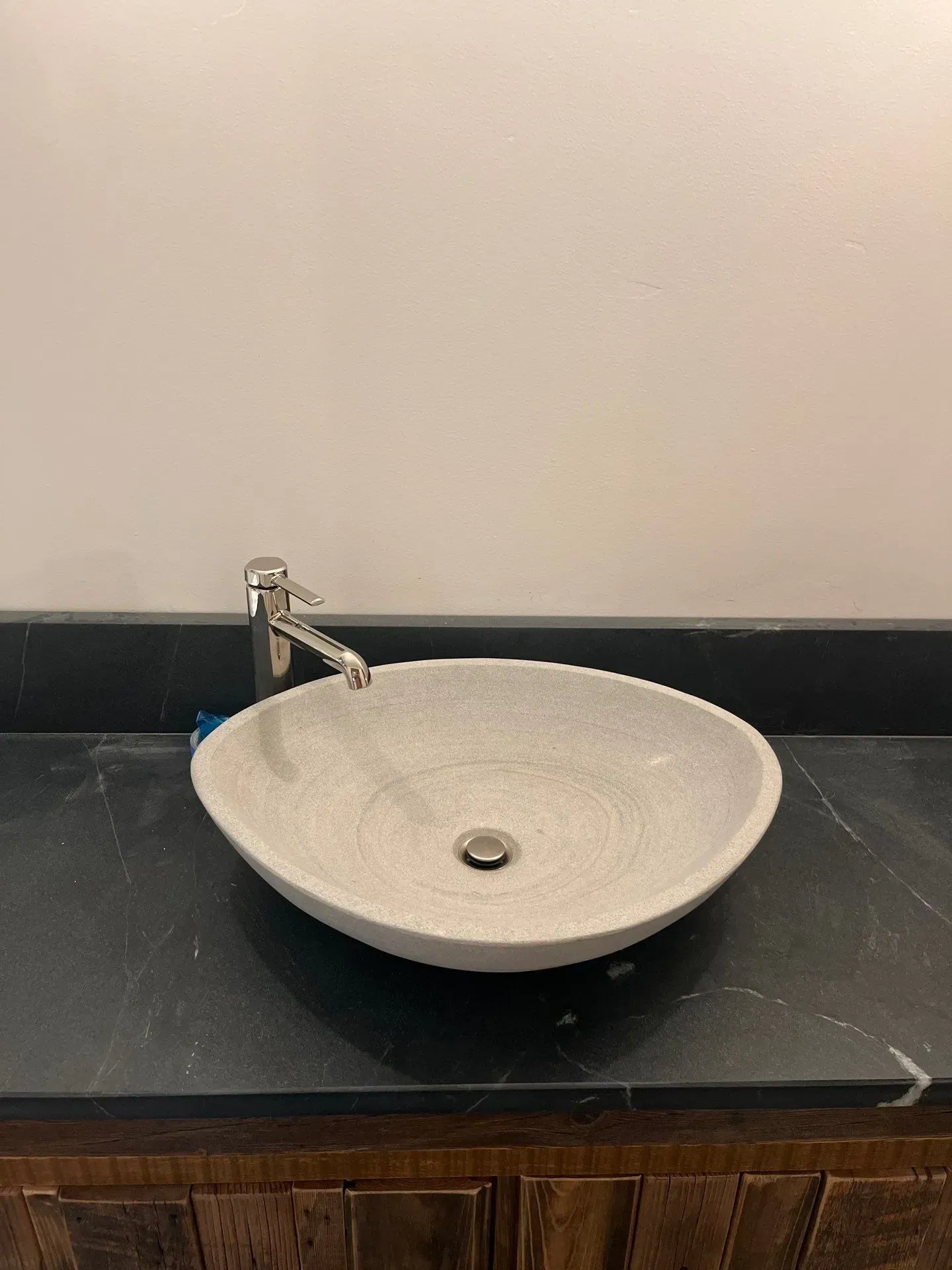 A speckled, light-gray stone vessel sink sits on a dark, marble countertop with a chrome faucet.