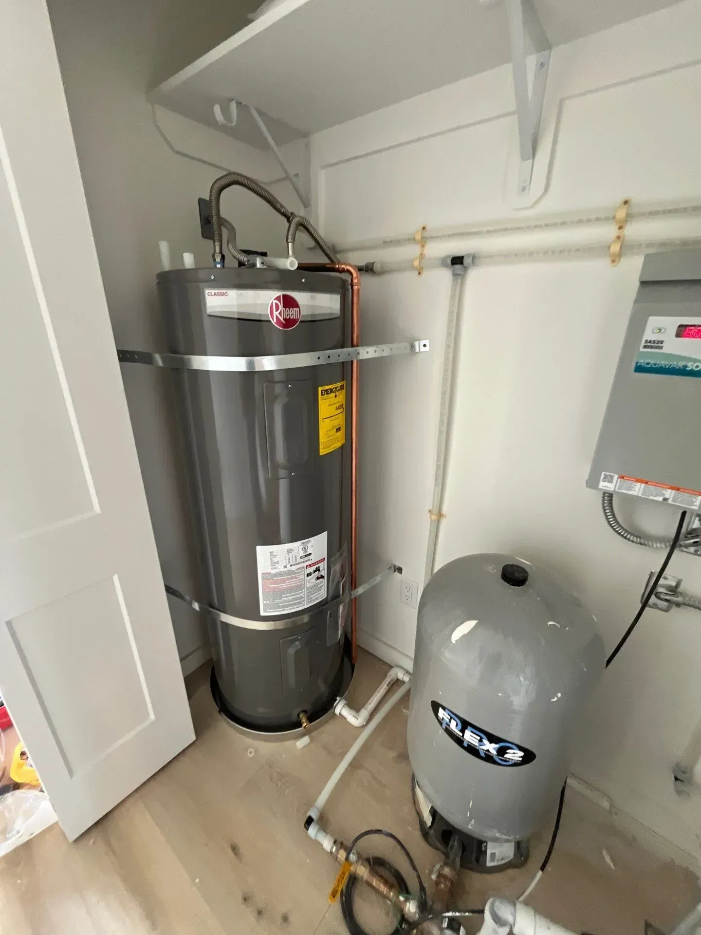 A water heater, expansion tank, and electrical panel are installed inside a small indoor utility closet.