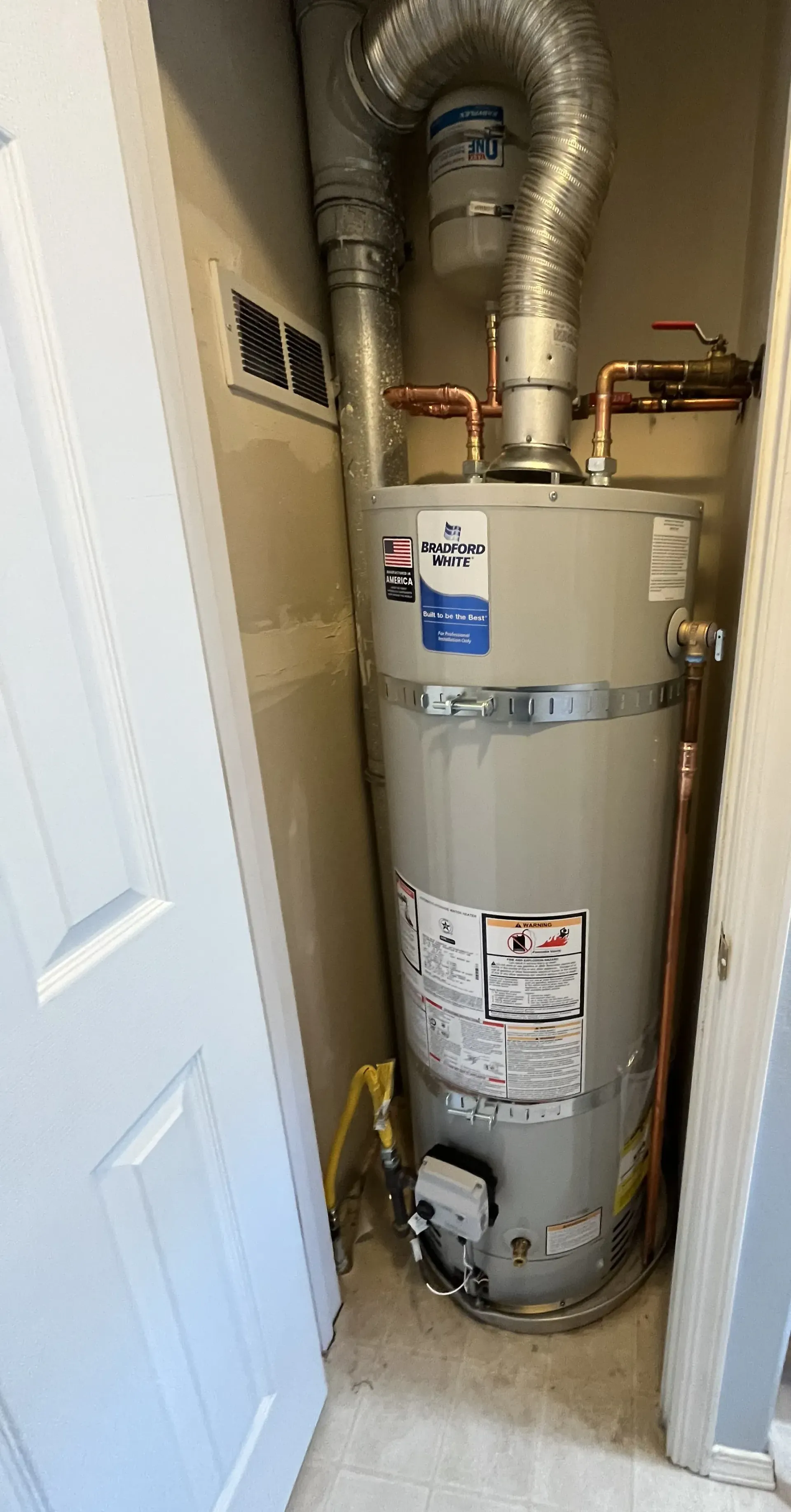 A gas water heater with metal venting installed in a narrow indoor closet.