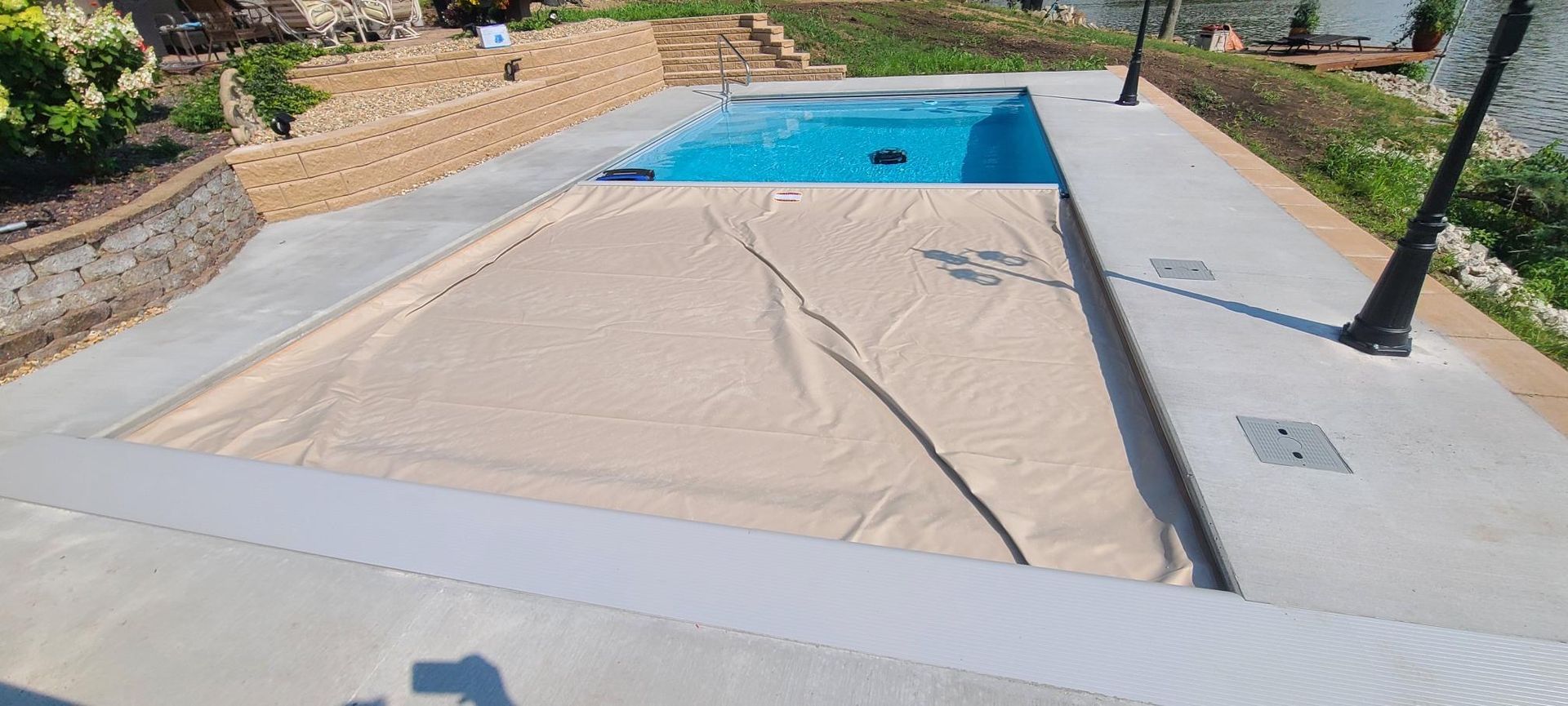 A rectangular pool with a tan cover. The pool has blue water. Concrete surrounds the pool.