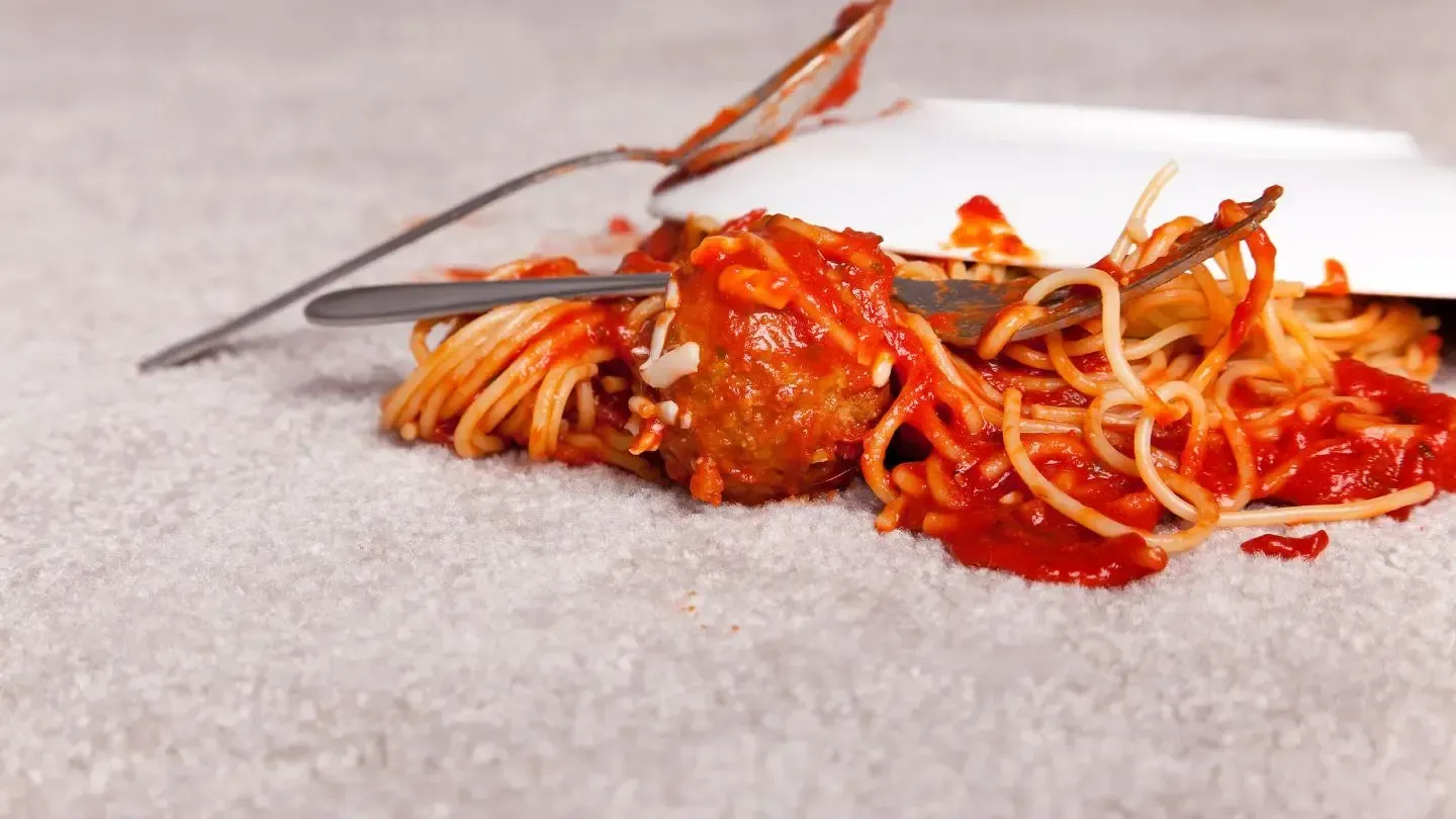 A plate of spaghetti and meatballs on a carpet with a fork.